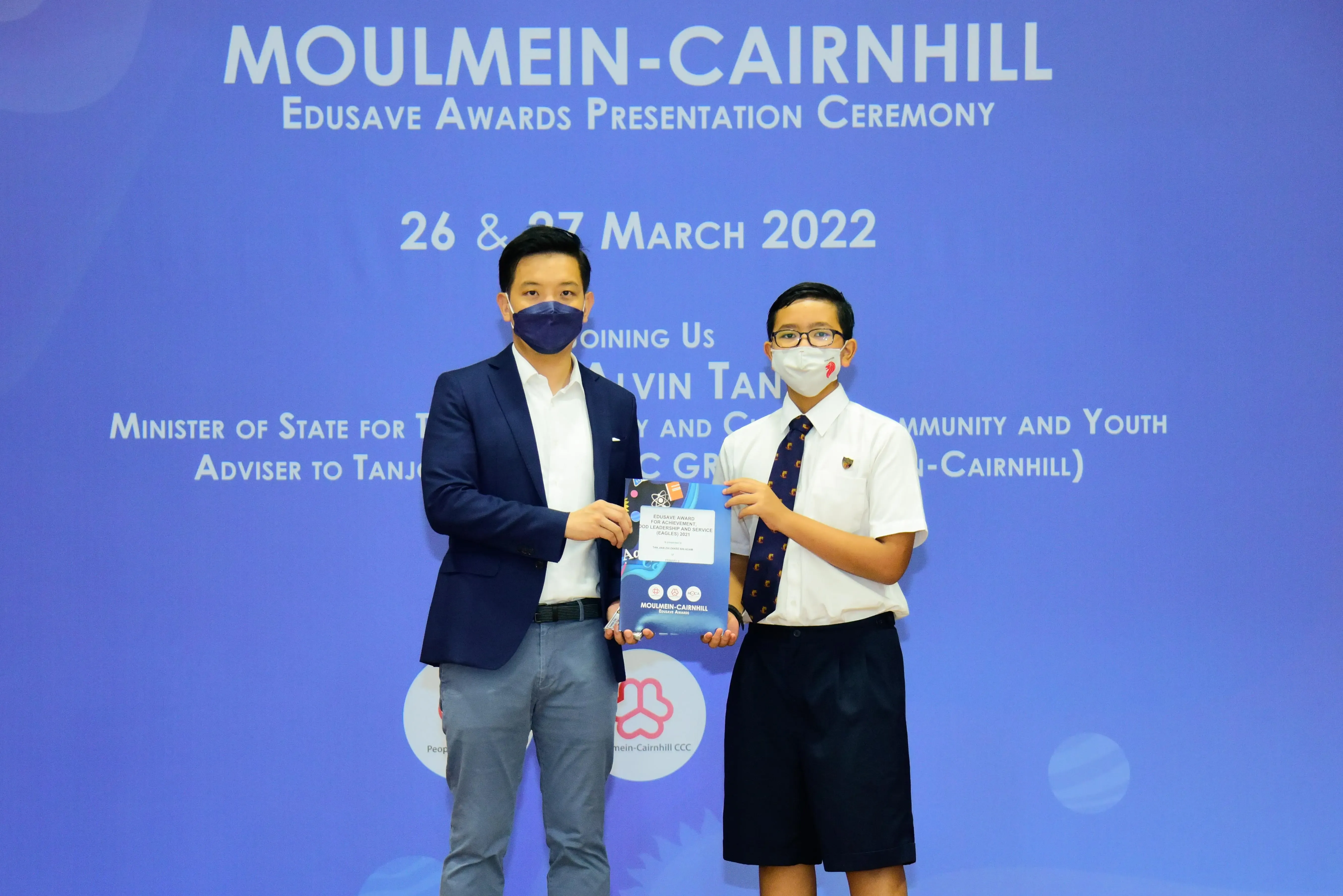 Two masked individuals hold an award booklet at the Moulmein-Cairnhill Edusave Awards Ceremony, March 2022.