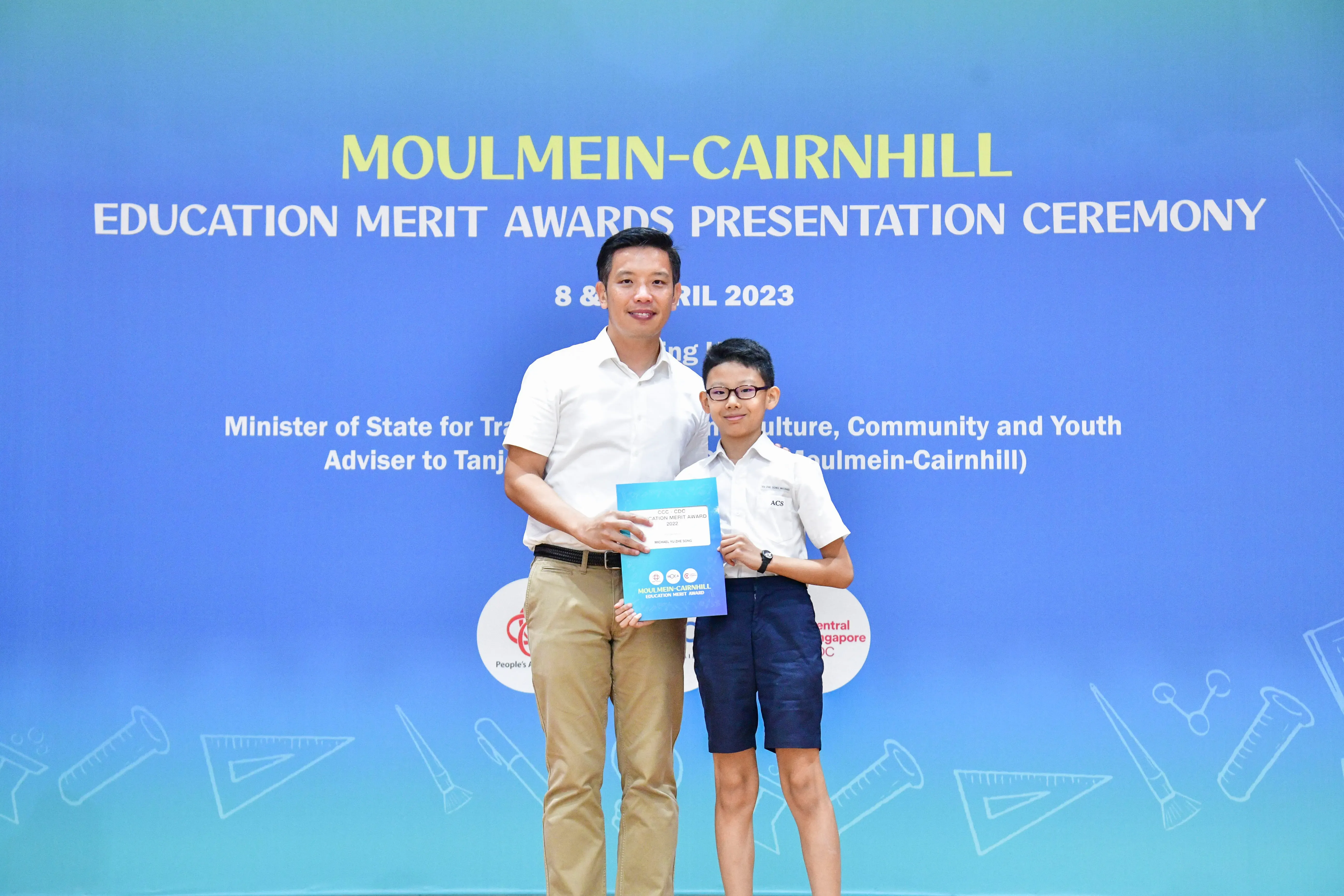 An adult and a young boy hold a certificate together at the Moulmein-Cairnhill Education Merit Awards Ceremony 2023.