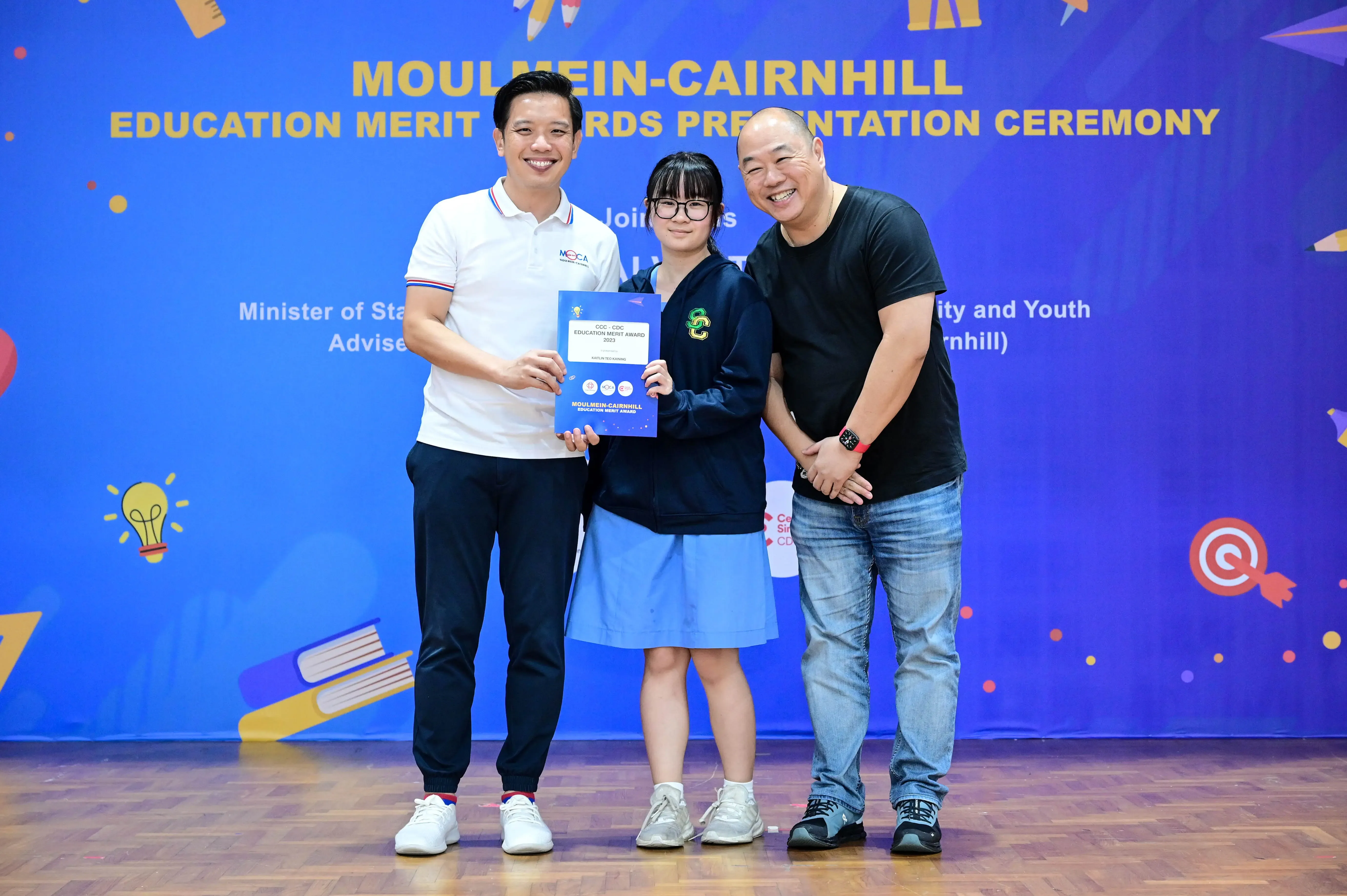 Three people pose with a certificate at the Moulmein-Cairnhill Education Merit Awards Presentation Ceremony.