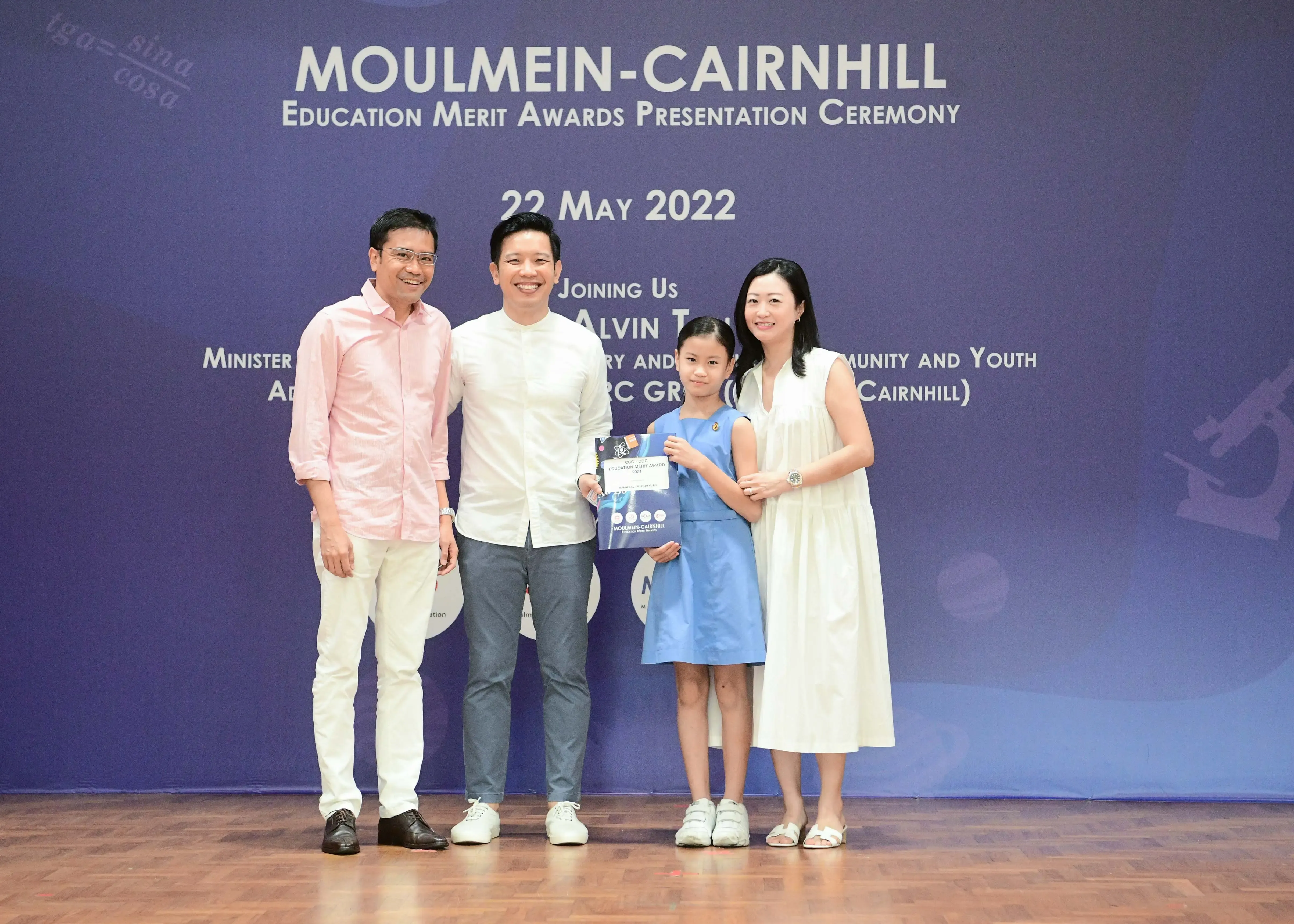 Four people pose at the Moulmein-Cairnhill Education Merit Awards Ceremony on 22 May 2022, a girl holding a certificate.