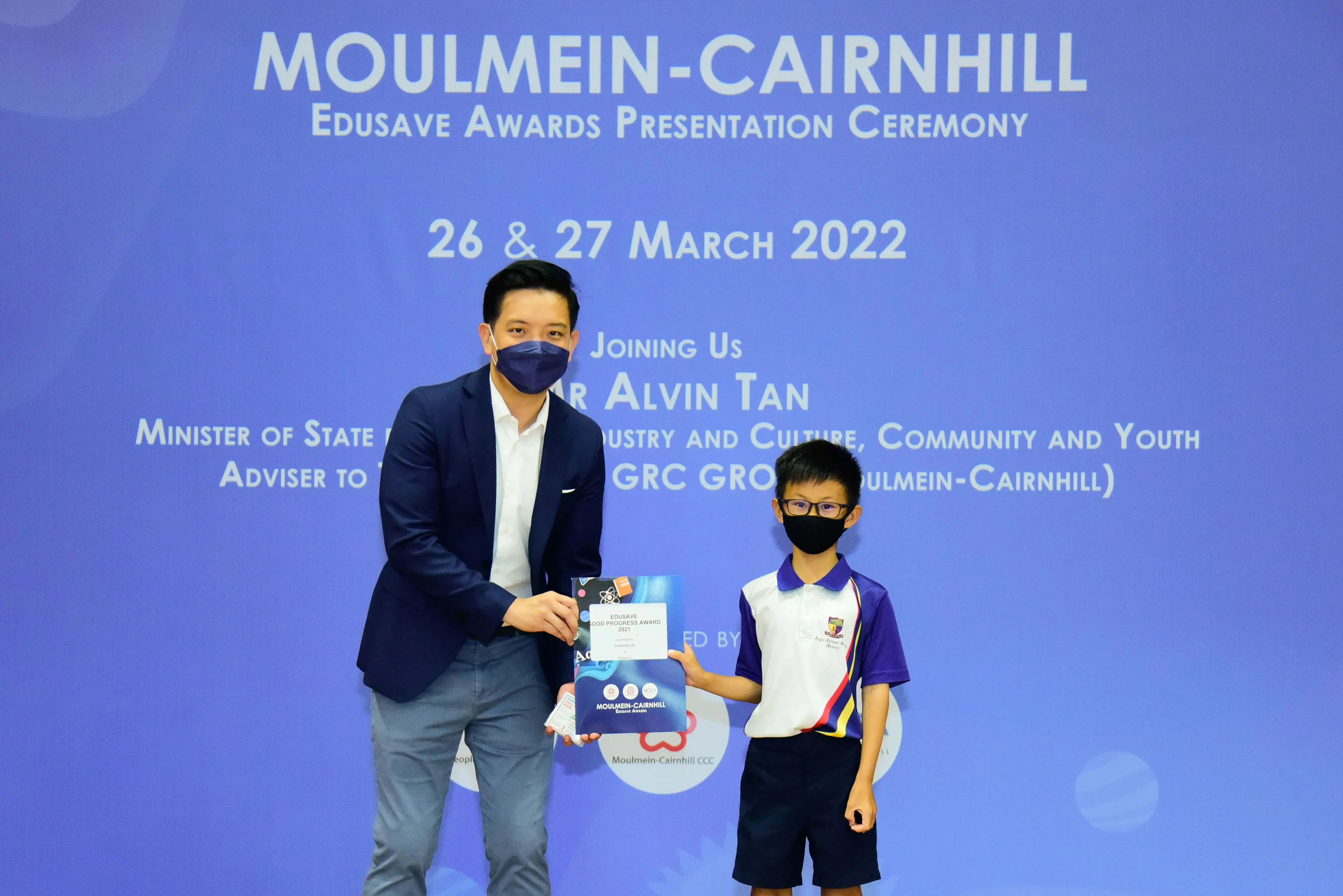 An adult and a young student in uniform hold an award together at the Moulmein-Cairnhill Edusave Awards Ceremony 2022.