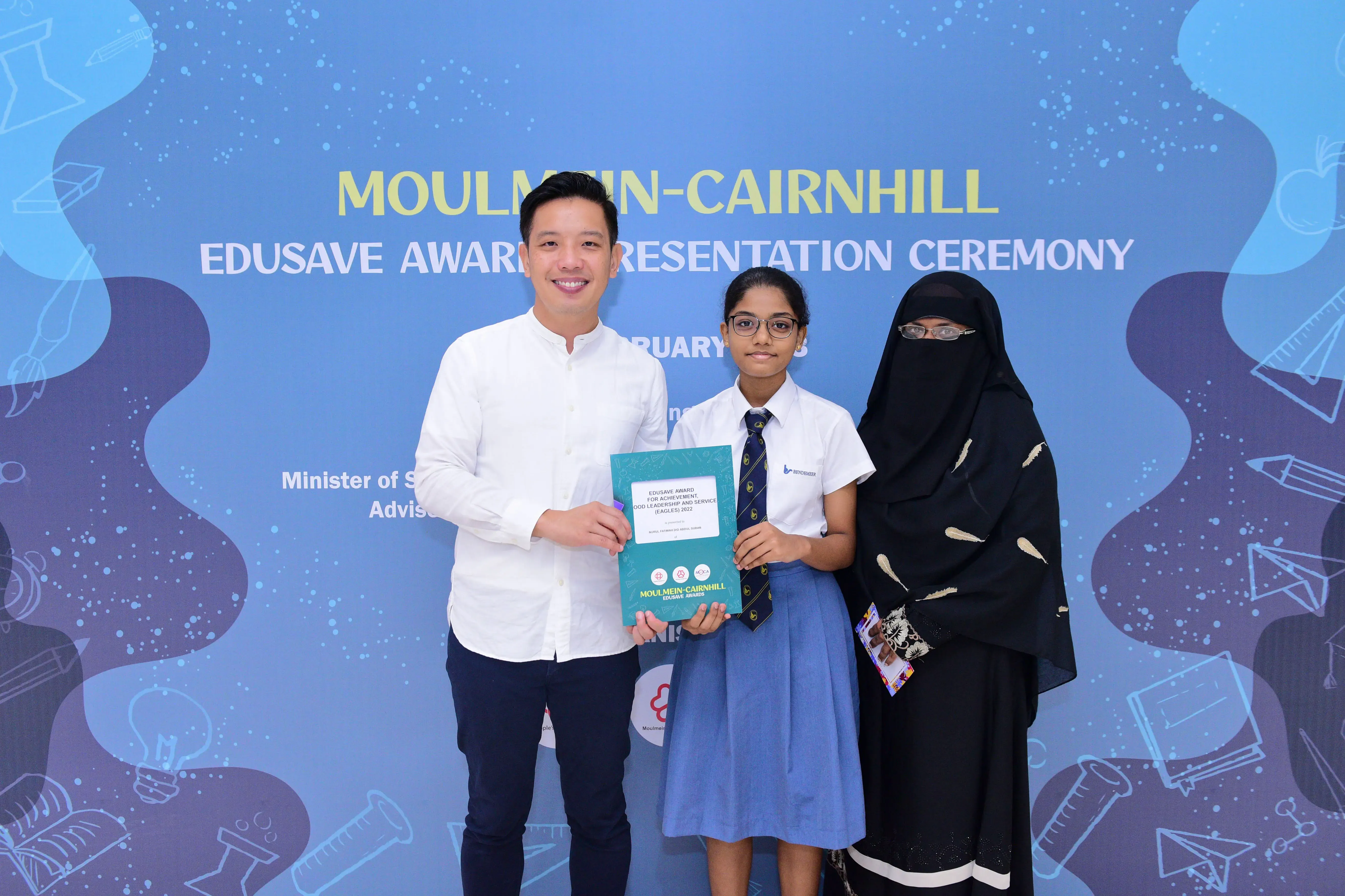Three people pose at the Moulmein-Cairnhill Edusave Award Presentation Ceremony, with a student holding a certificate.