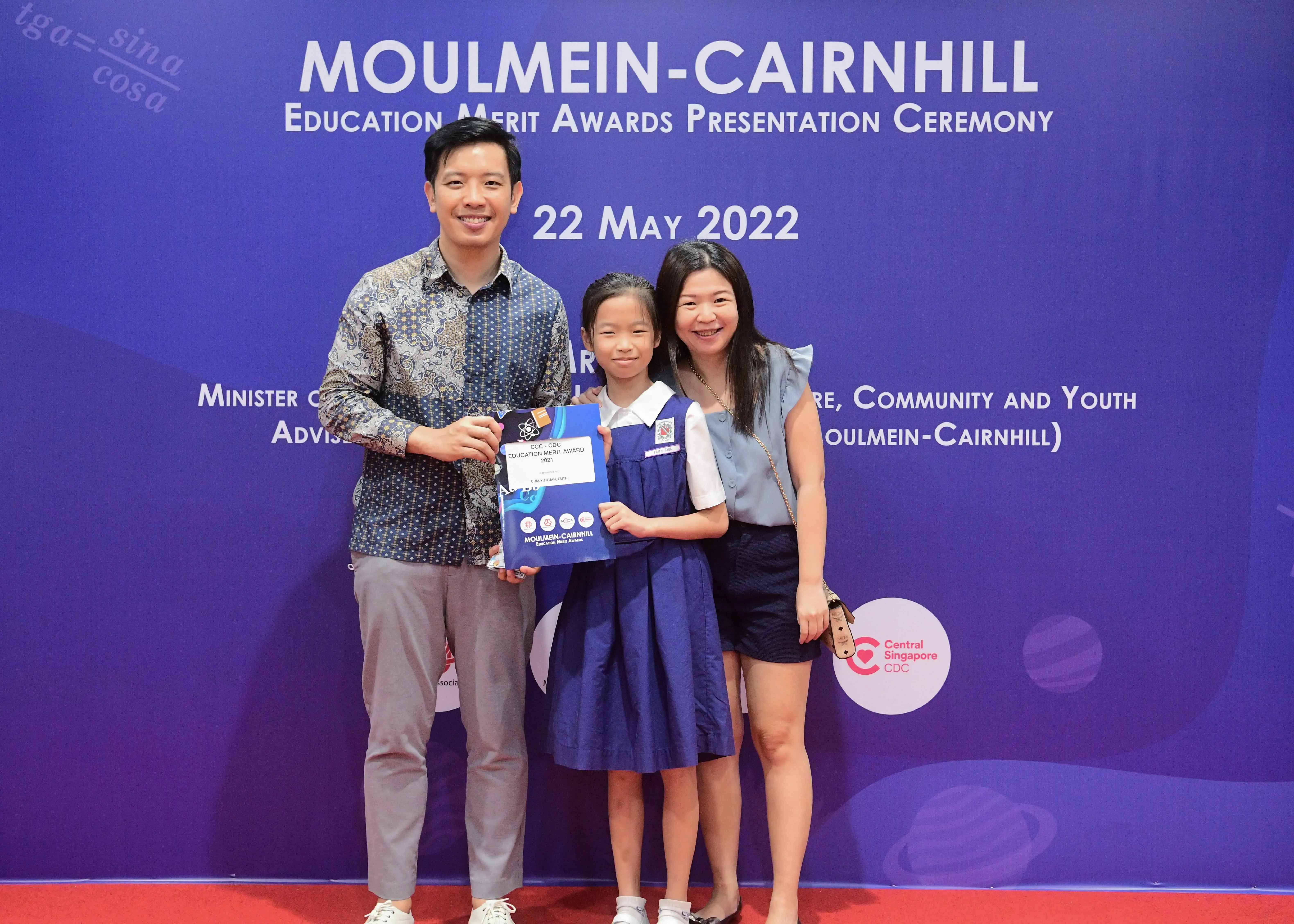 Two adults and a girl holding an award certificate pose at the Moulmein-Cairnhill Education Merit Awards on 22 May 2022.