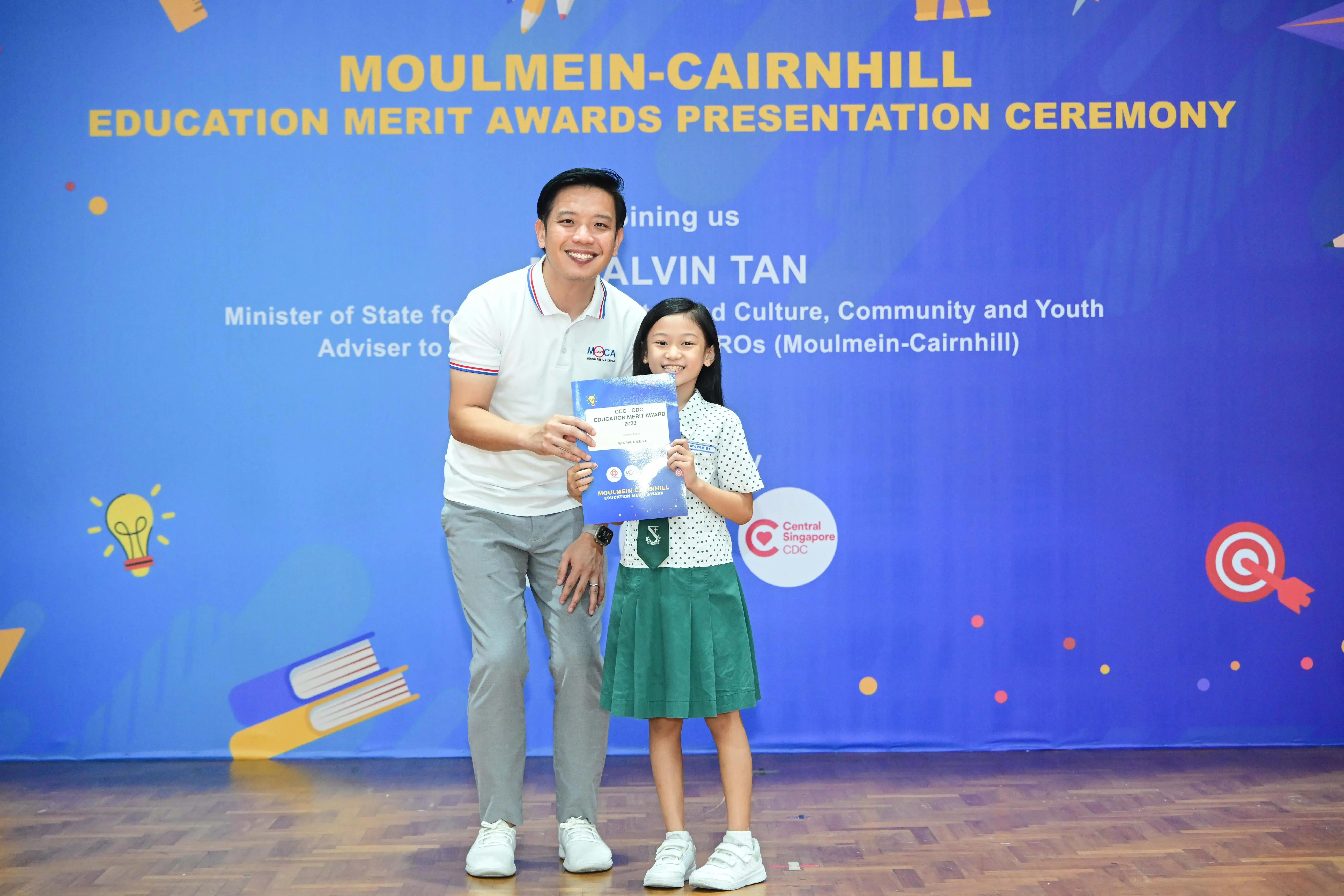 Man and young girl hold a certificate at the Moulmein-Cairnhill Education Merit Awards Presentation Ceremony.