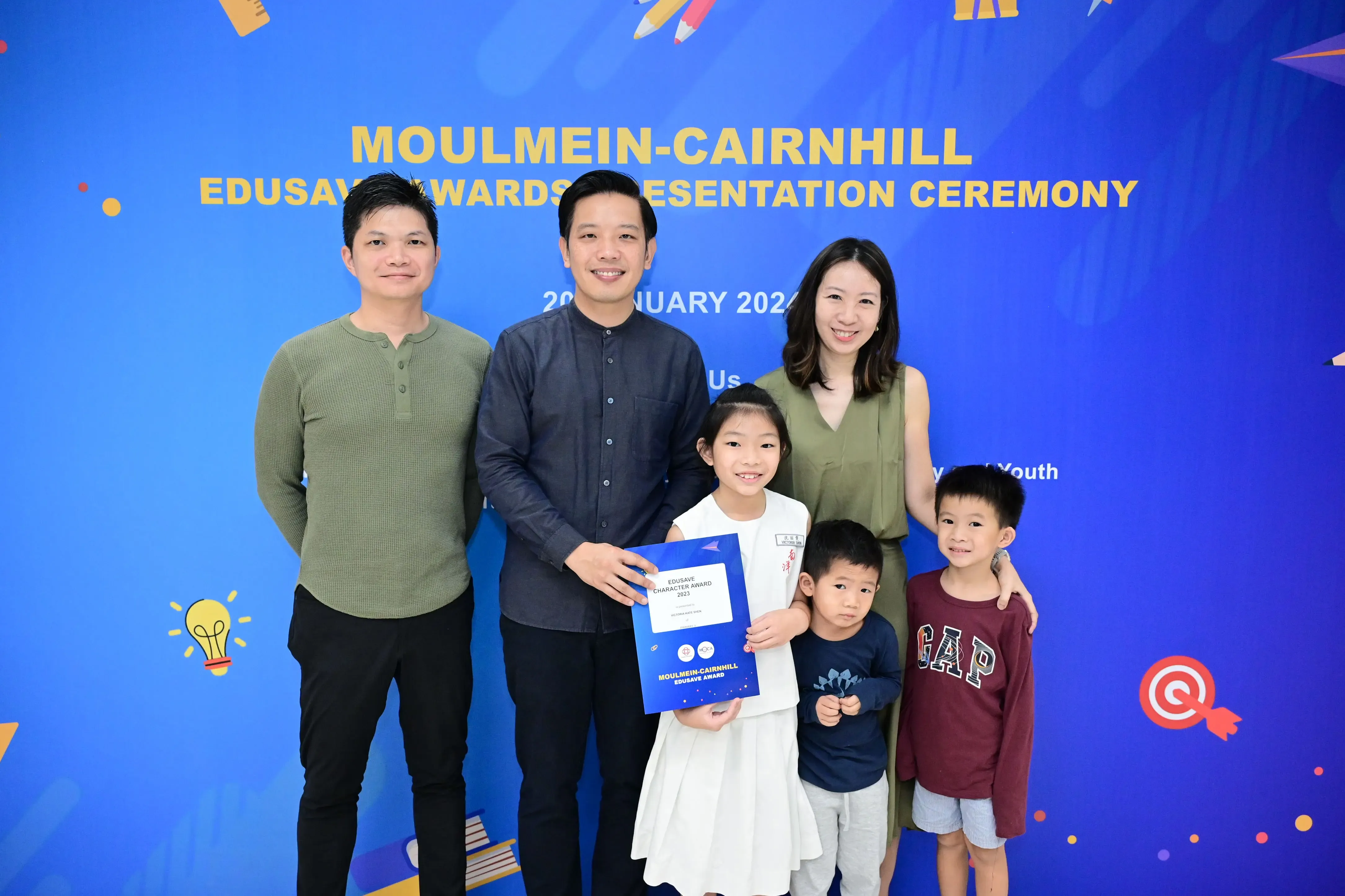 Family of five posing with an Edusave award certificate at Moulmein-Cairnhill Awards Presentation Ceremony 2024.
