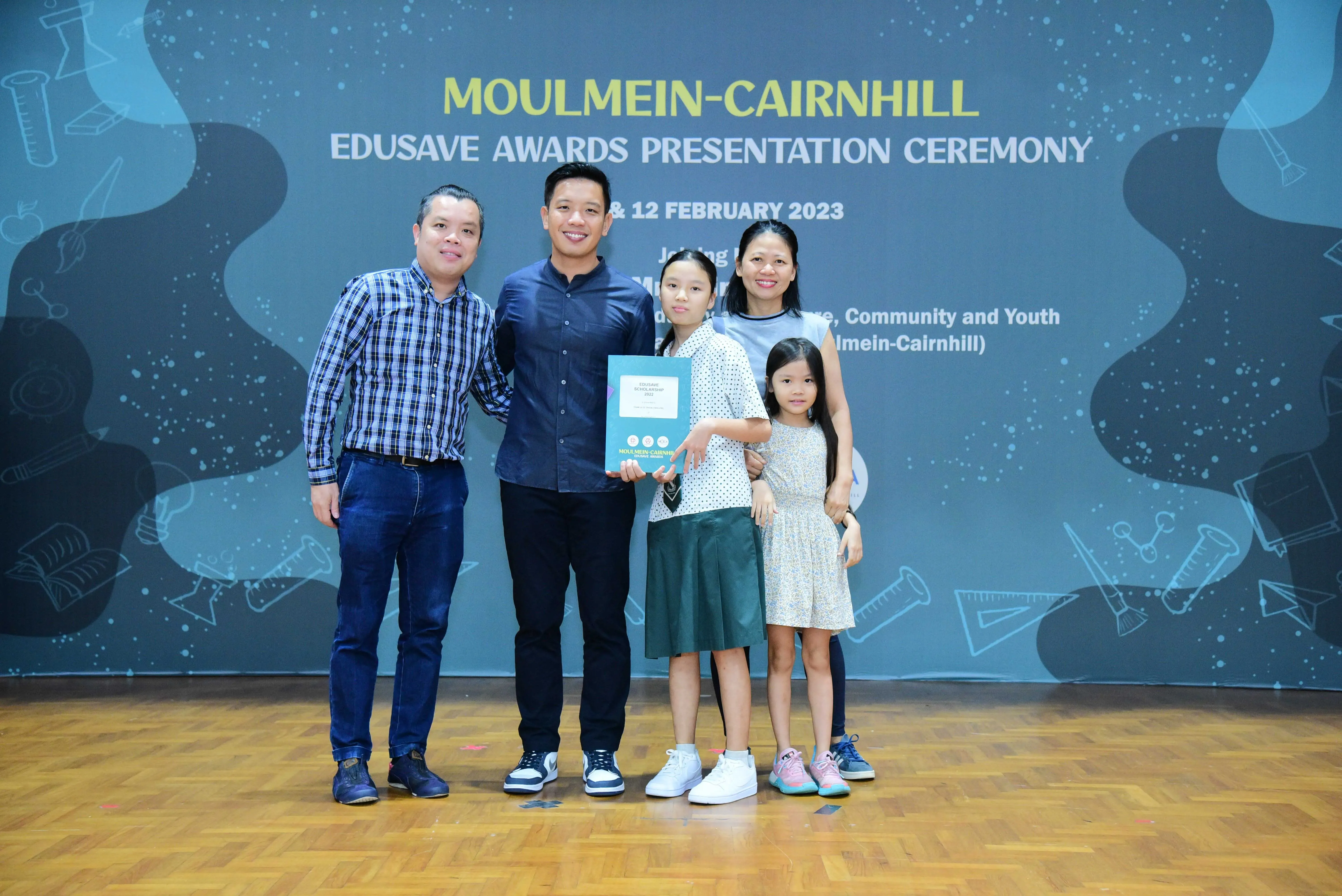 Five people pose with an award booklet at the Moulmein-Cairnhill Edusave Awards Presentation Ceremony, February 2023.