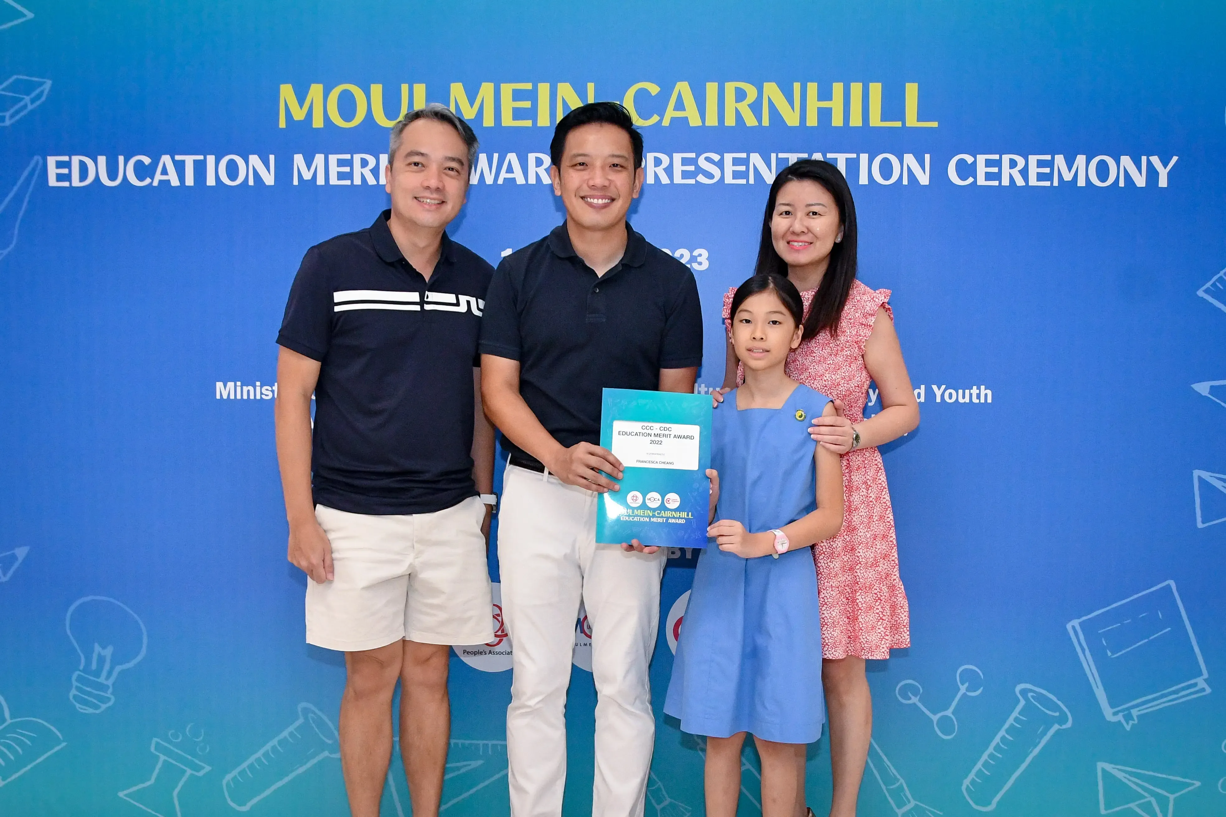 Three adults and a girl pose holding an award certificate at the Moulmein-Cairnhill Education Merit Award Presentation Ceremony.
