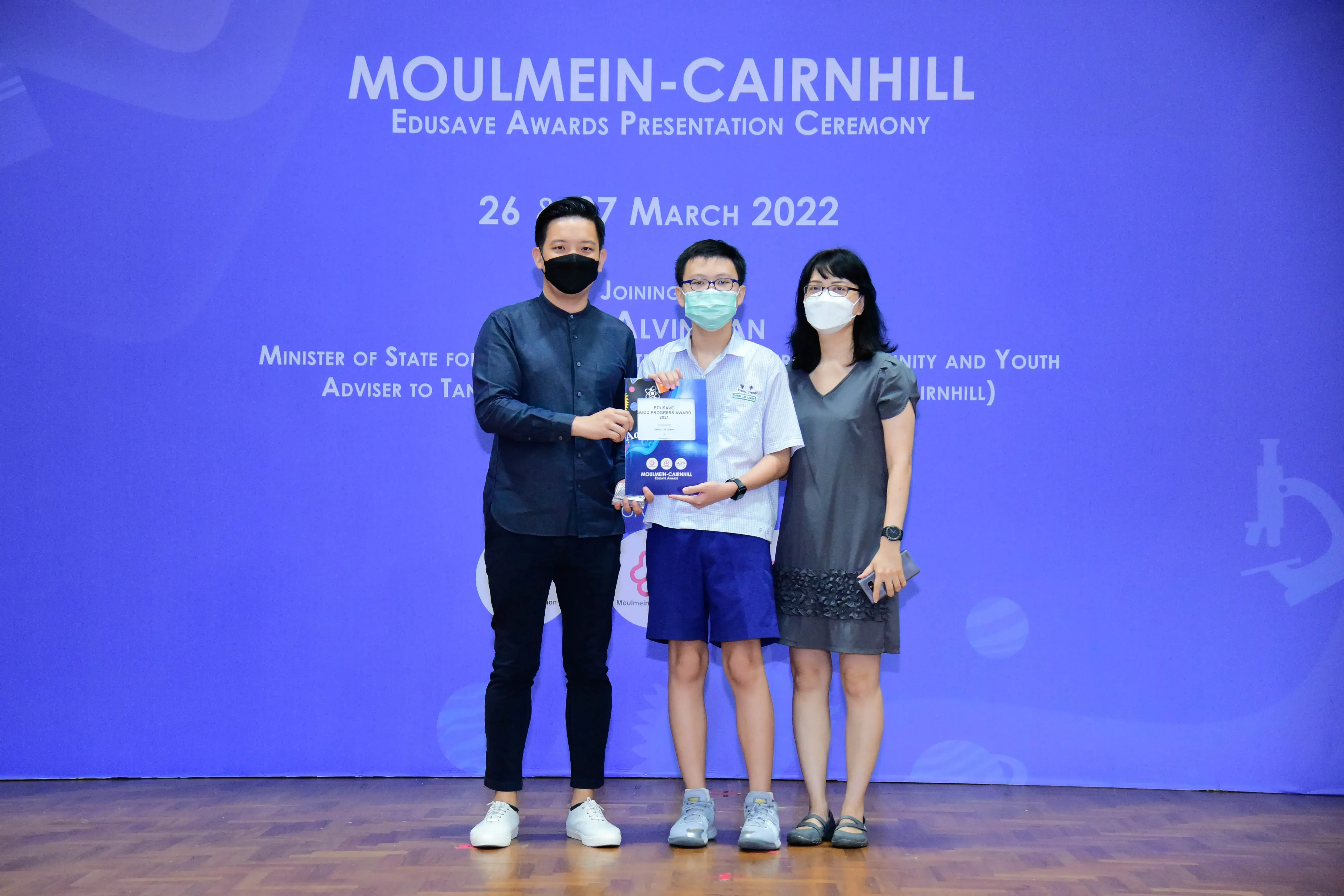 Three masked people pose with an award at the Moulmein-Cairnhill Edusave Awards Ceremony, March 2022.