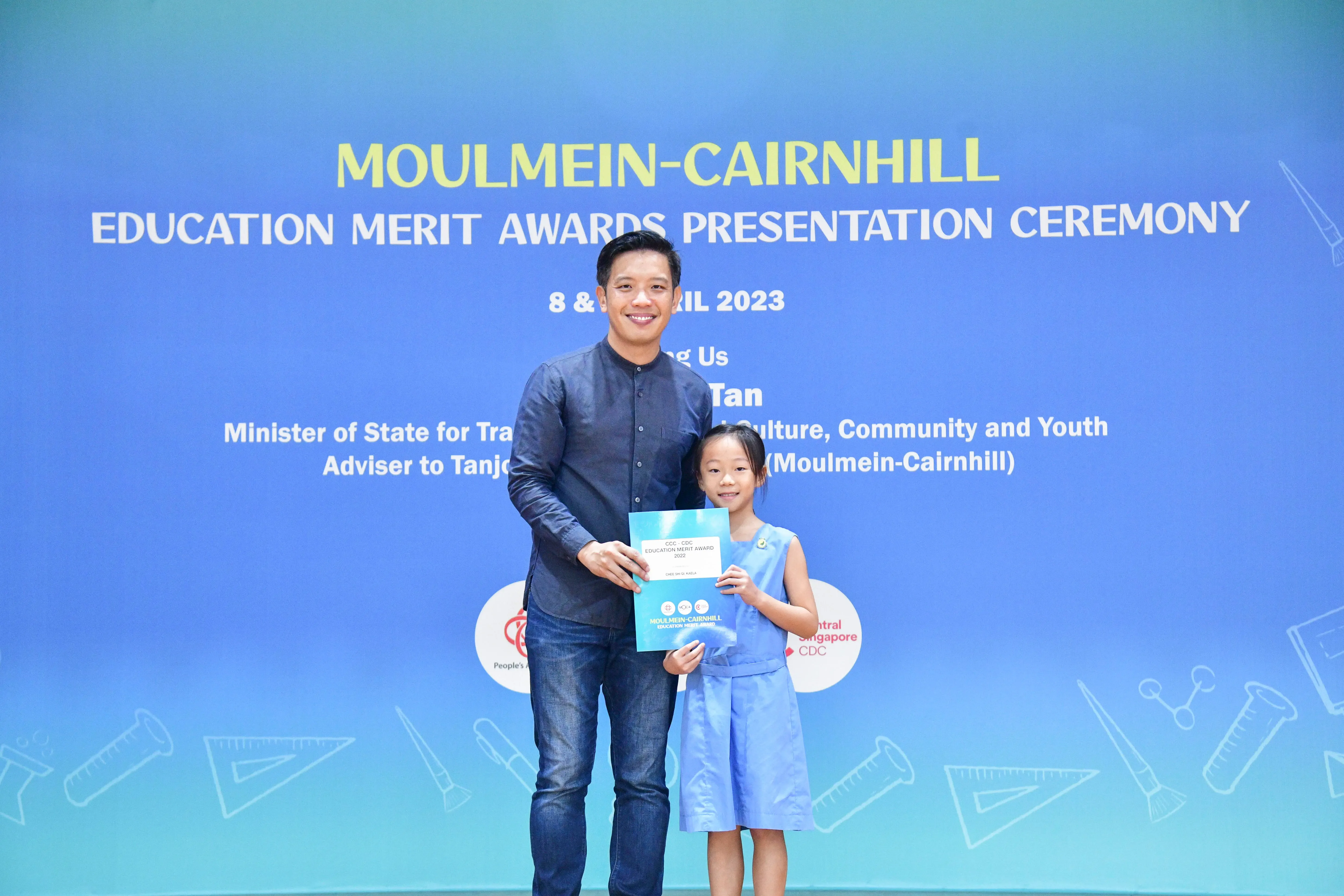 A man and a young girl hold a certificate together at the Moulmein-Cairnhill Education Merit Awards Ceremony 2023.