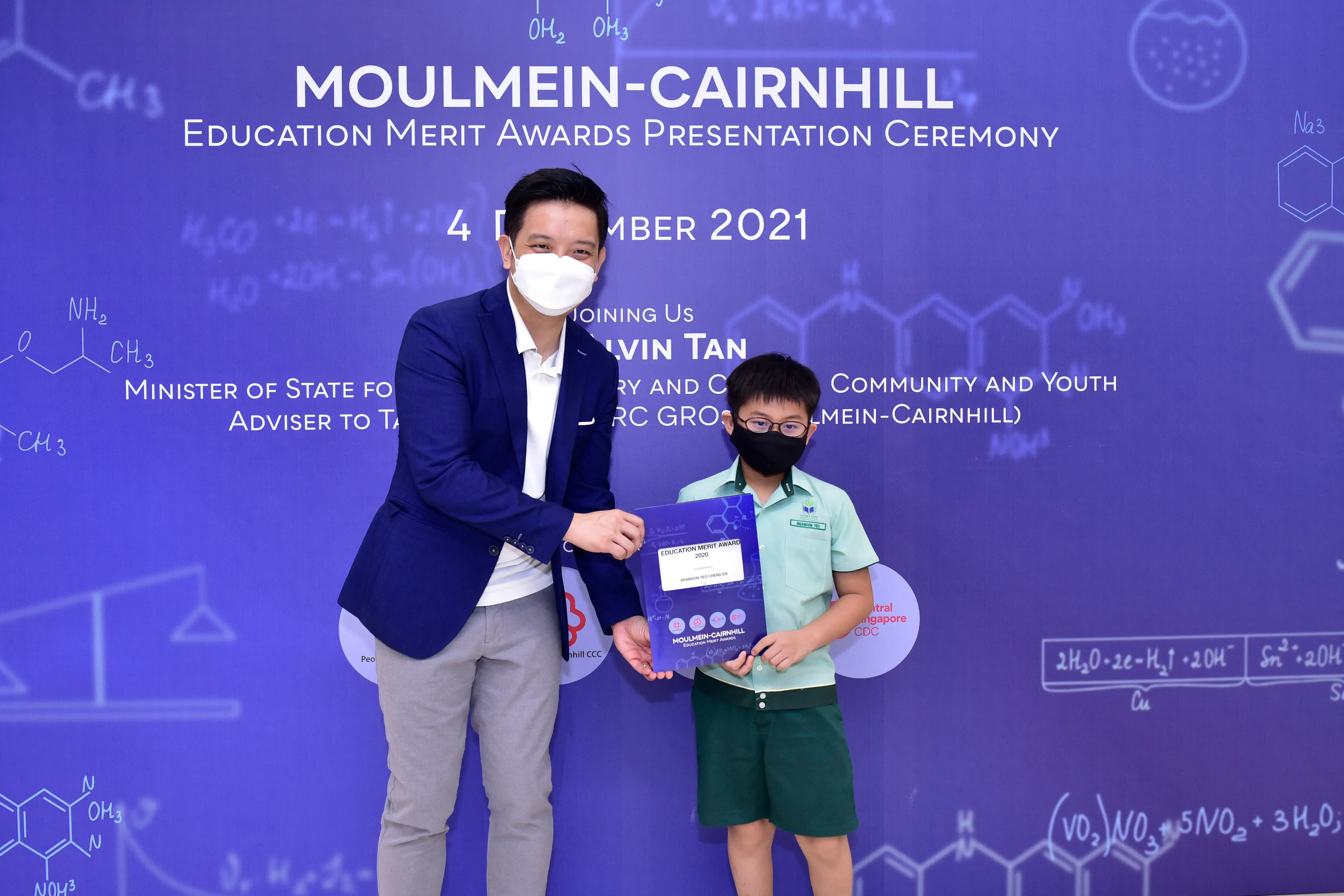 An adult and a masked child hold an award certificate at the Moulmein-Cairnhill Education Merit Awards Ceremony, 4 December 2021.
