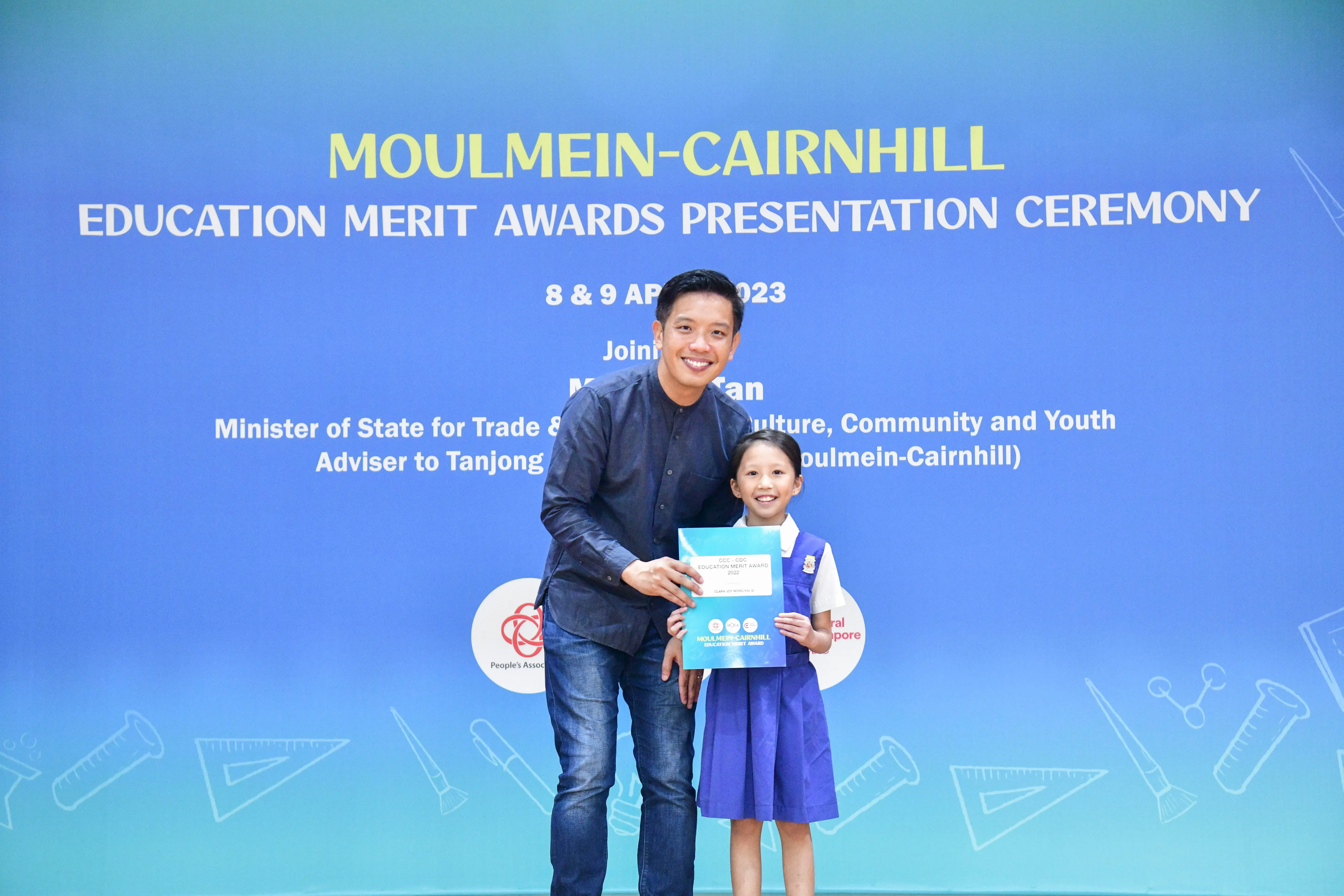 A man and a young girl hold an award certificate at the Moulmein-Cairnhill Education Merit Awards Ceremony 2023.