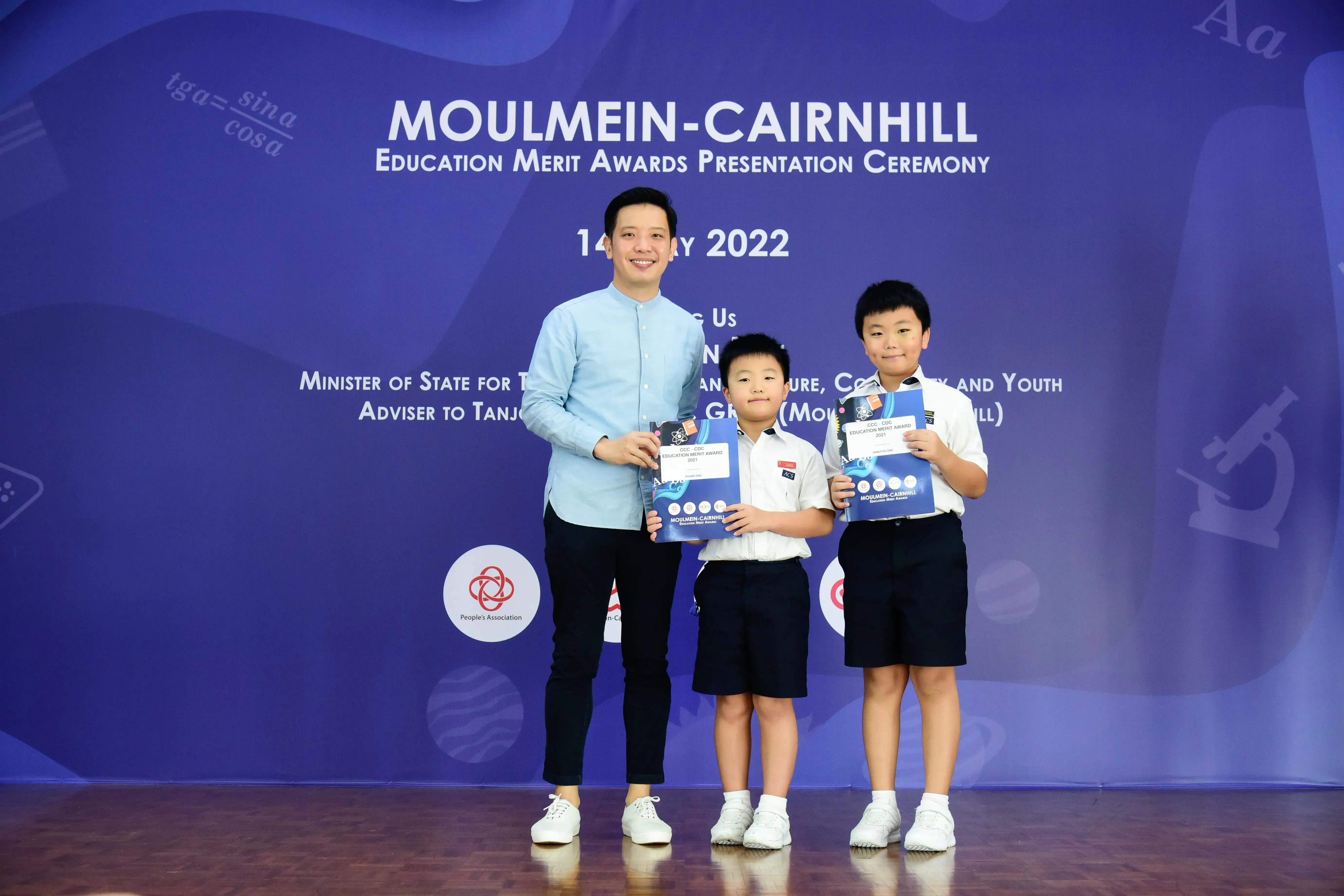 An adult and two young students hold awards at the Moulmein-Cairnhill Education Merit Awards Ceremony 2022.