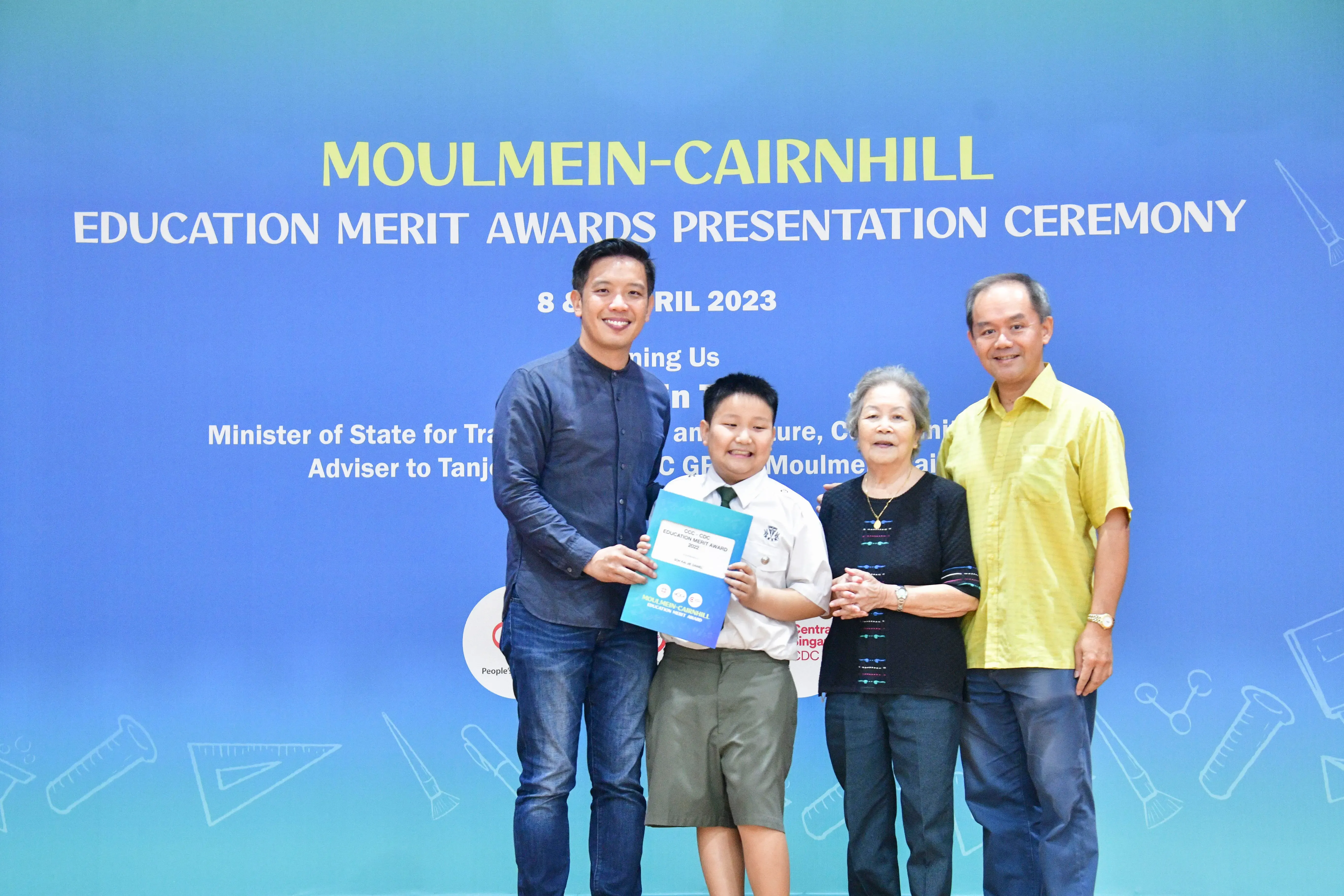 A boy holding an award certificate poses with three adults at the Moulmein-Cairnhill Education Merit Awards 2023.