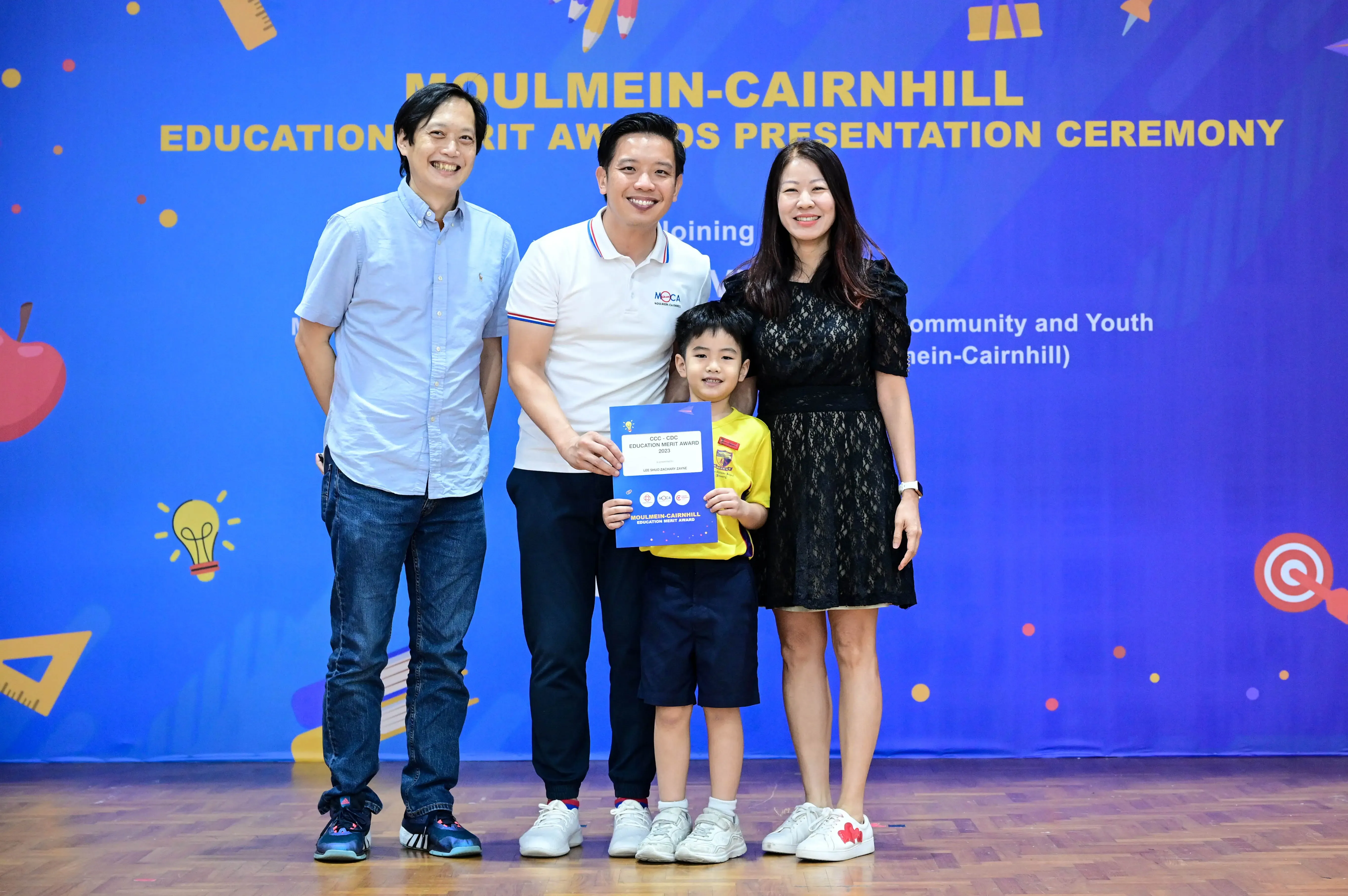Three adults and a young boy pose with an award certificate at the Moulmein-Cairnhill Education Merit Awards ceremony.