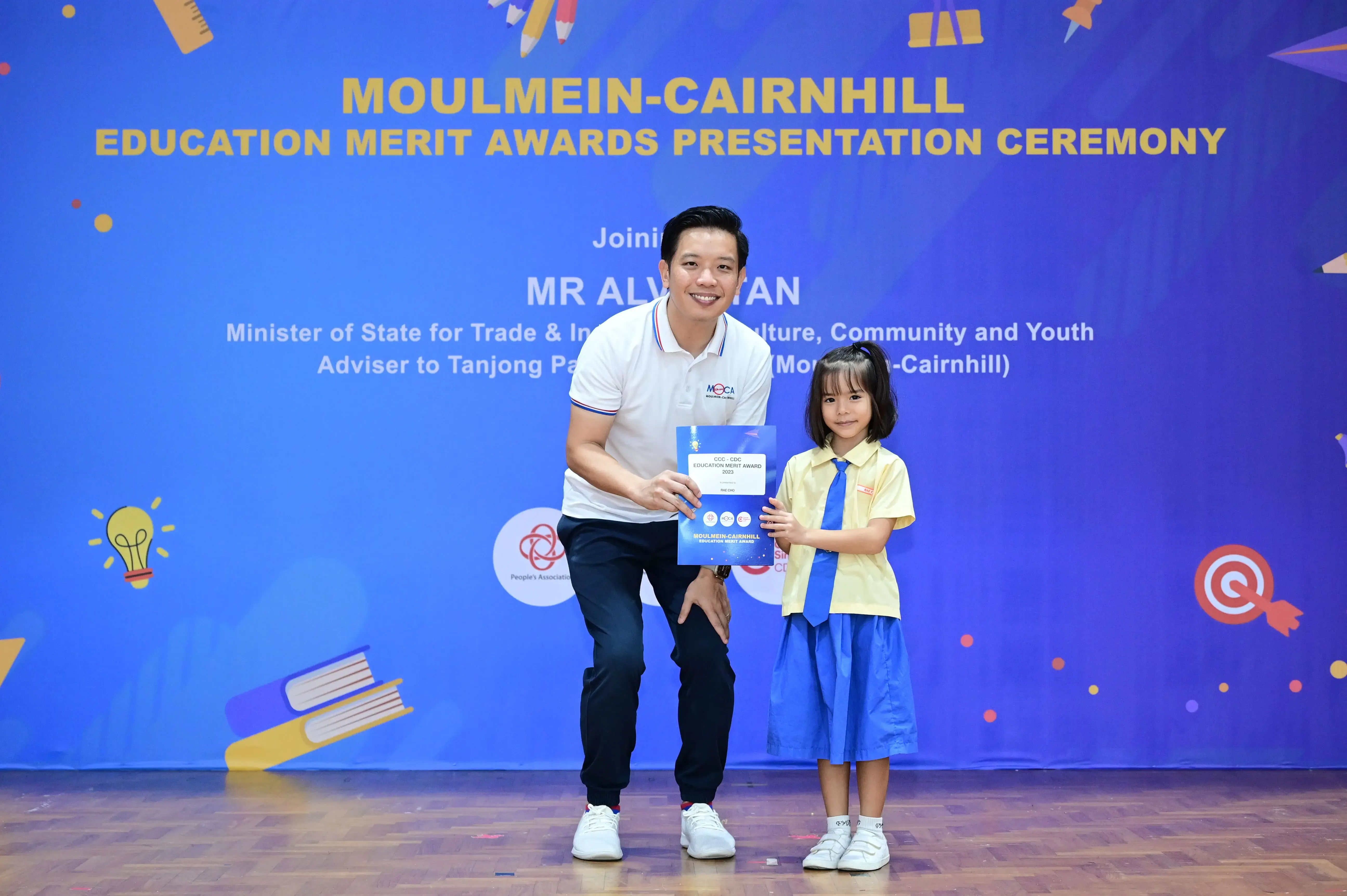 A man and a young girl hold an award certificate at the Moulmein-Cairnhill Education Merit Awards ceremony.