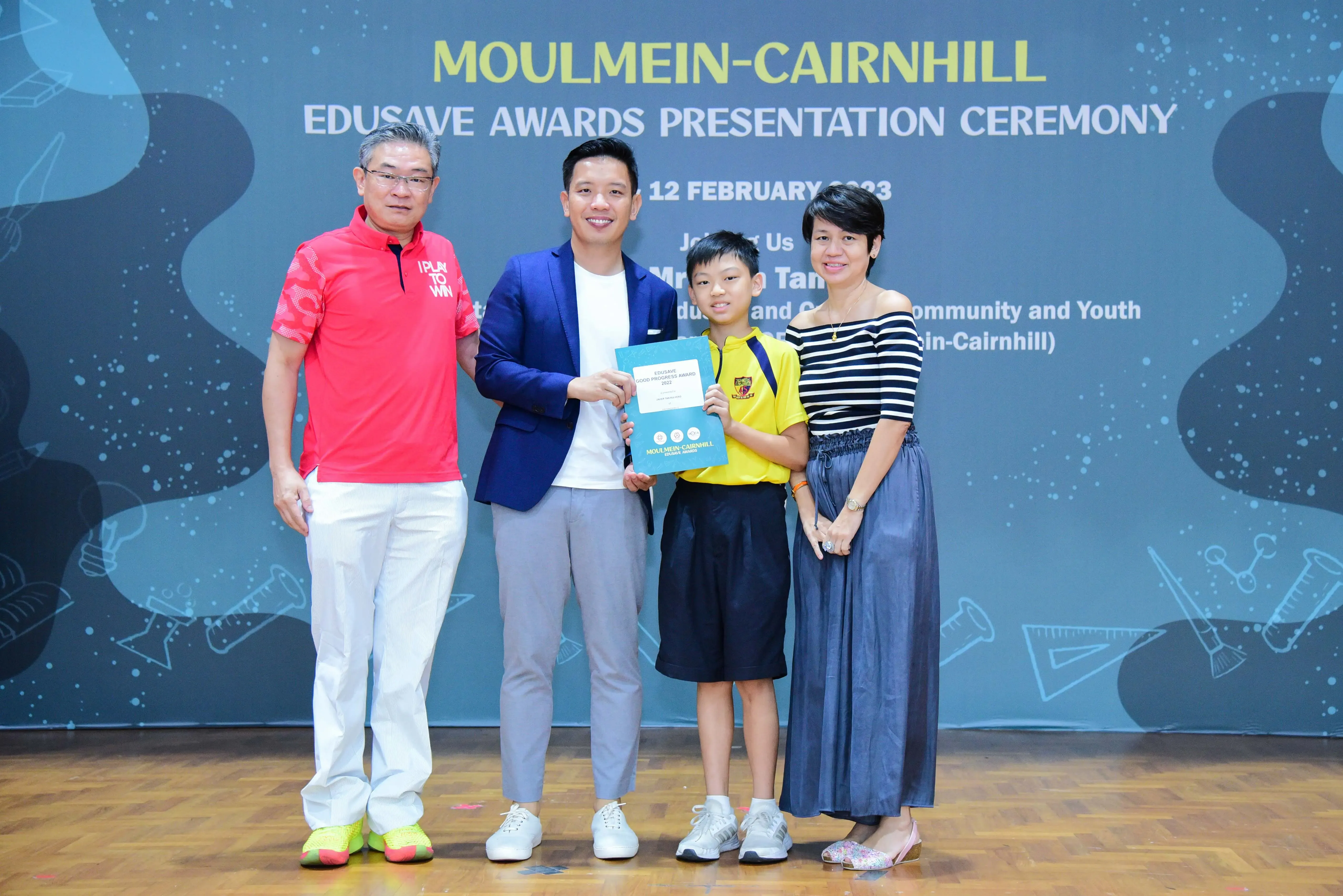 Four people pose at the Moulmein-Cairnhill Edusave Awards Presentation Ceremony, with a boy holding an award certificate.