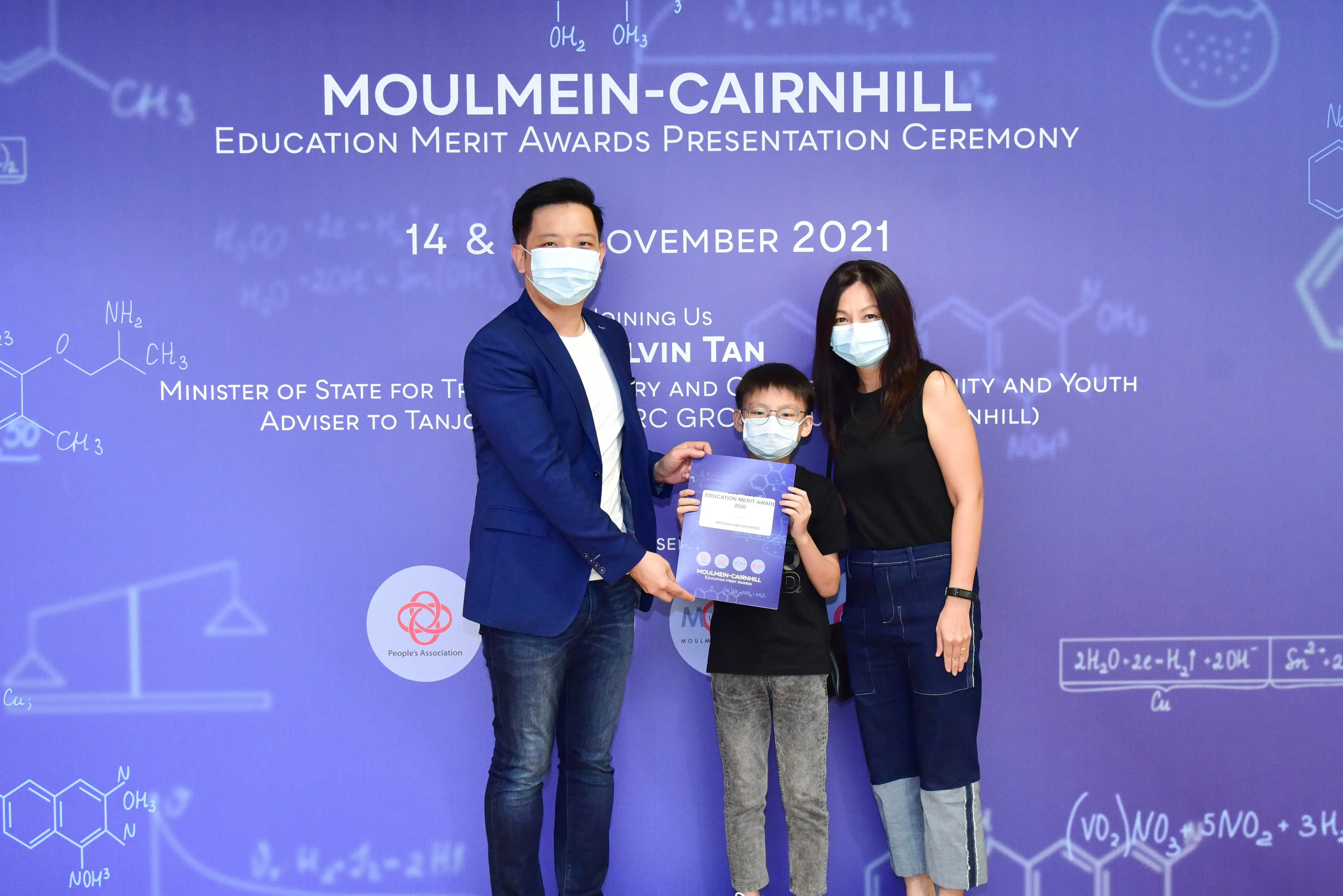 Three masked people pose with an award certificate at the Moulmein-Cairnhill Education Merit Awards Ceremony, November 2021.