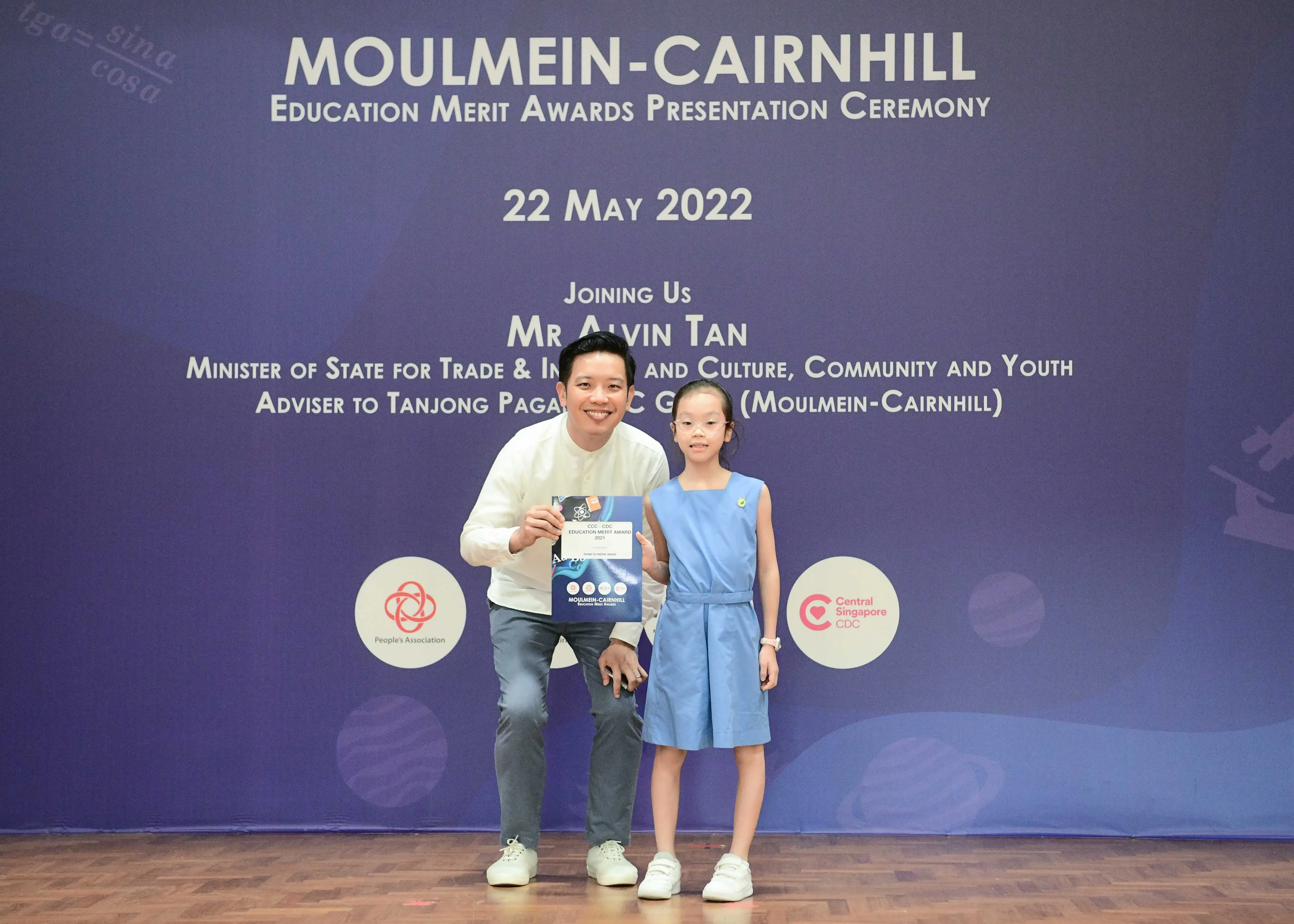 A man and a young girl pose together holding an award certificate at the Moulmein-Cairnhill Education Merit Awards ceremony.