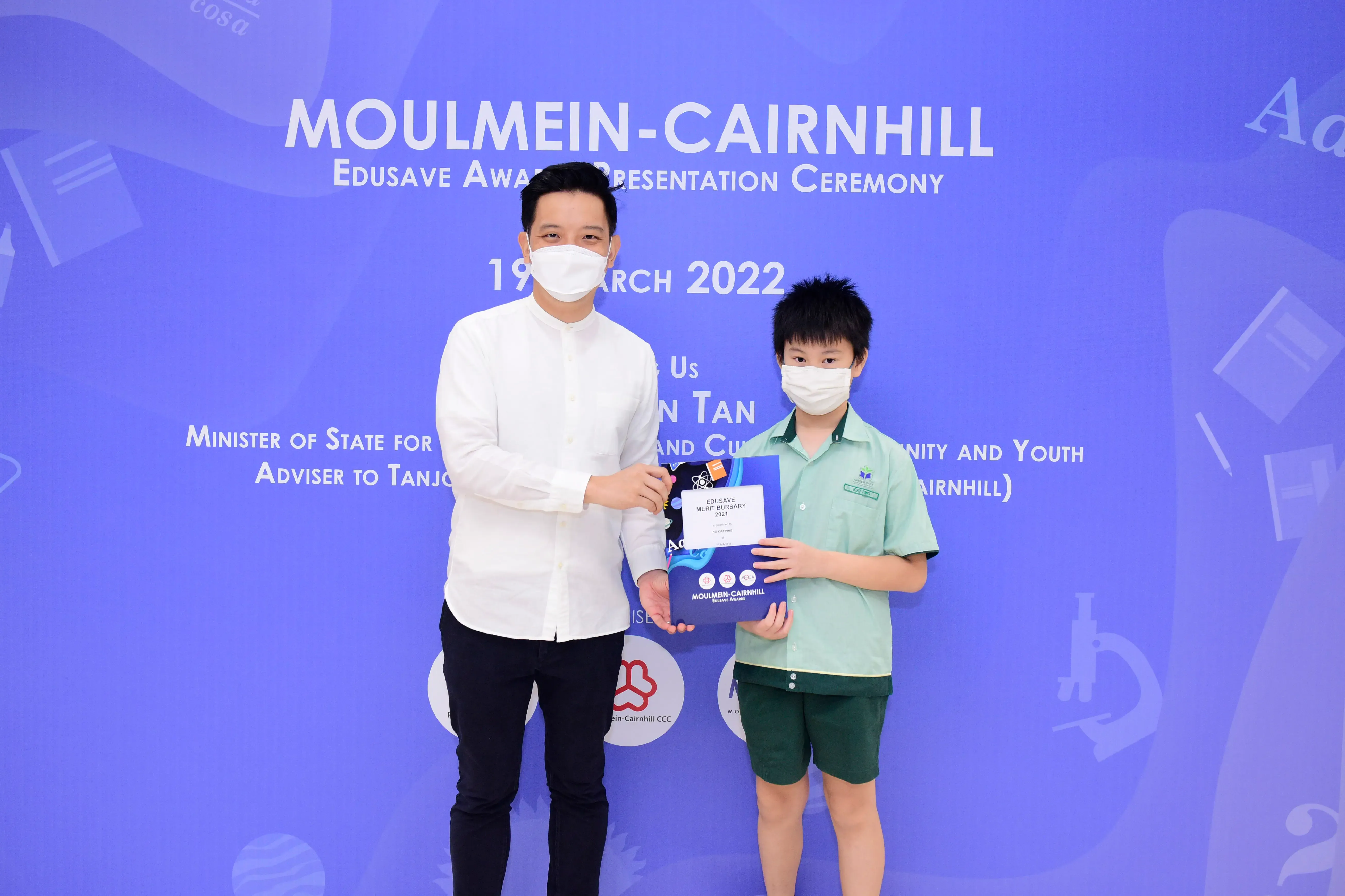 An adult and a young boy wearing masks hold an Edusave Merit Bursary certificate at the Moulmein-Cairnhill ceremony.
