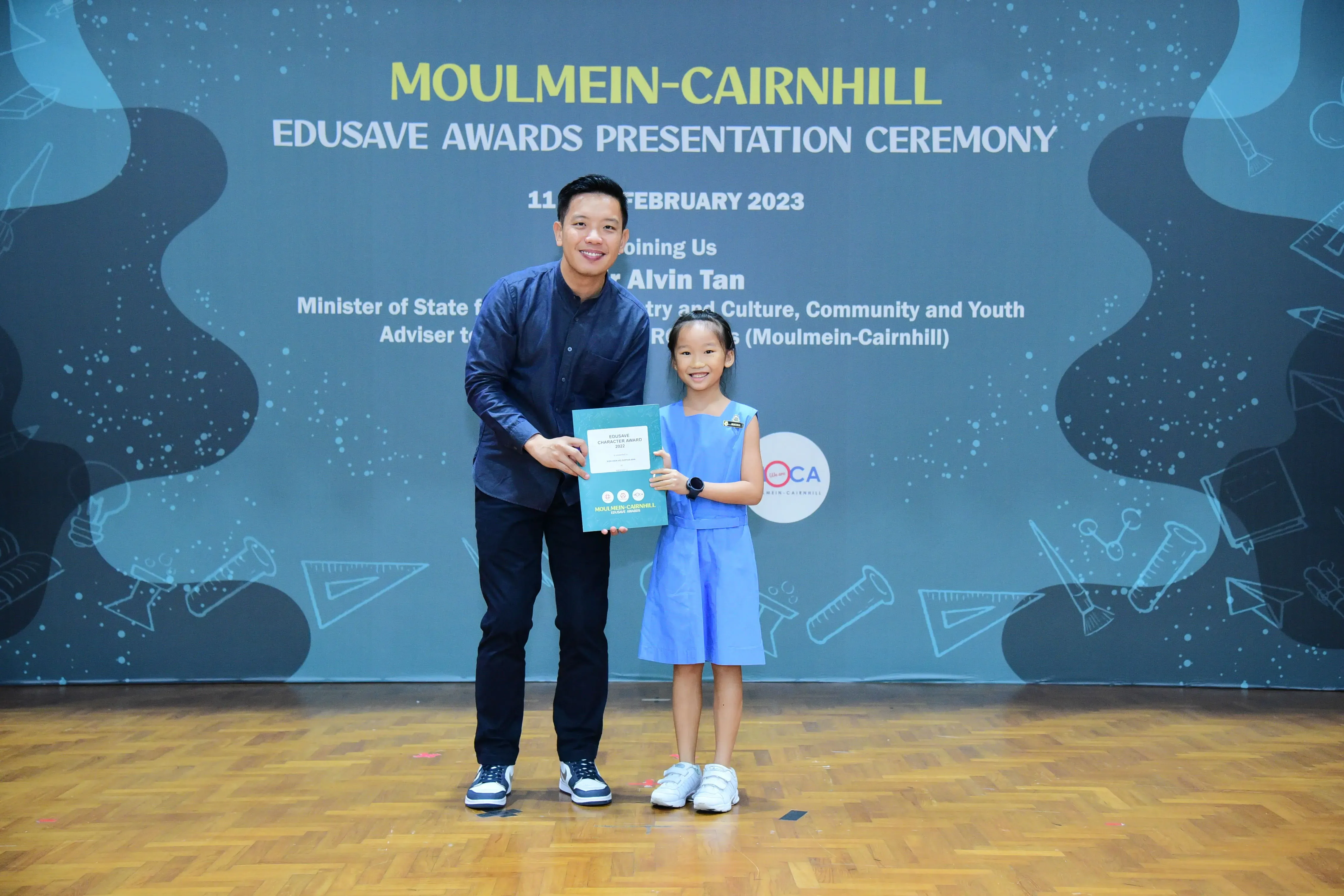 A man and a young girl hold a certificate at the Moulmein-Cairnhill Edusave Awards Presentation Ceremony, February 2023.