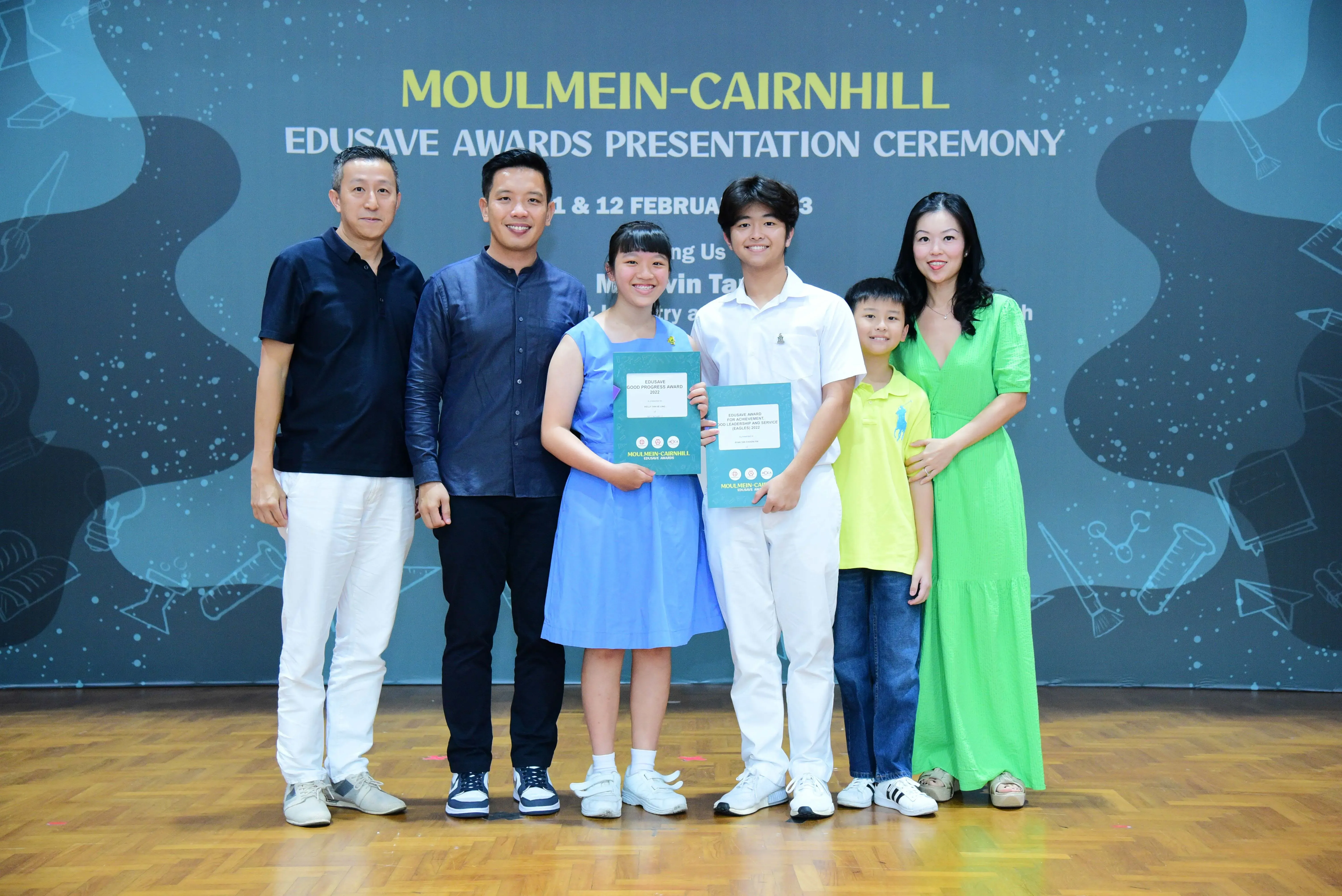 Six people pose at the Moulmein-Cairnhill Edusave Awards Presentation Ceremony, two children holding award certificates.