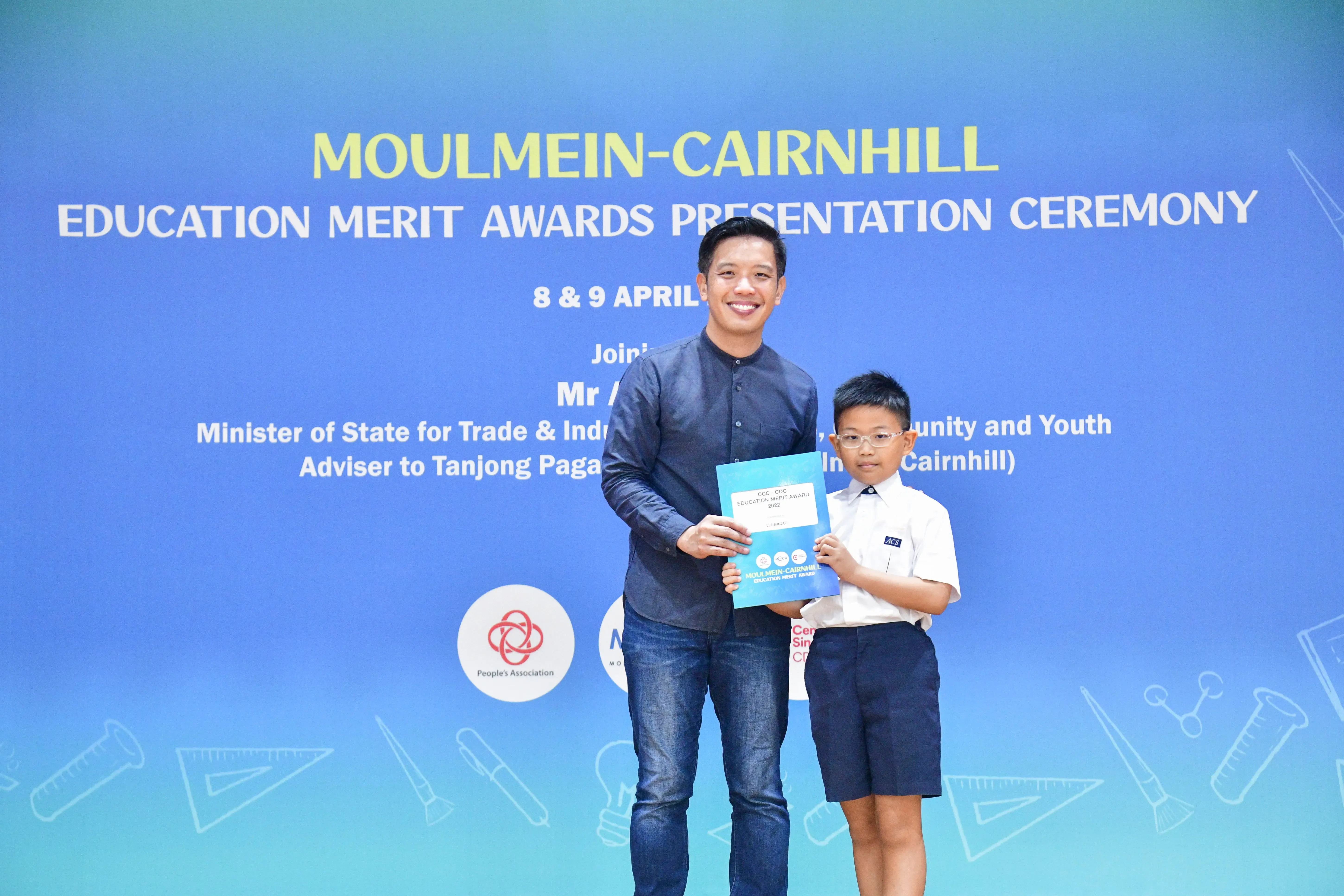A man and a young boy hold a certificate at the Moulmein-Cairnhill Education Merit Awards Presentation Ceremony.