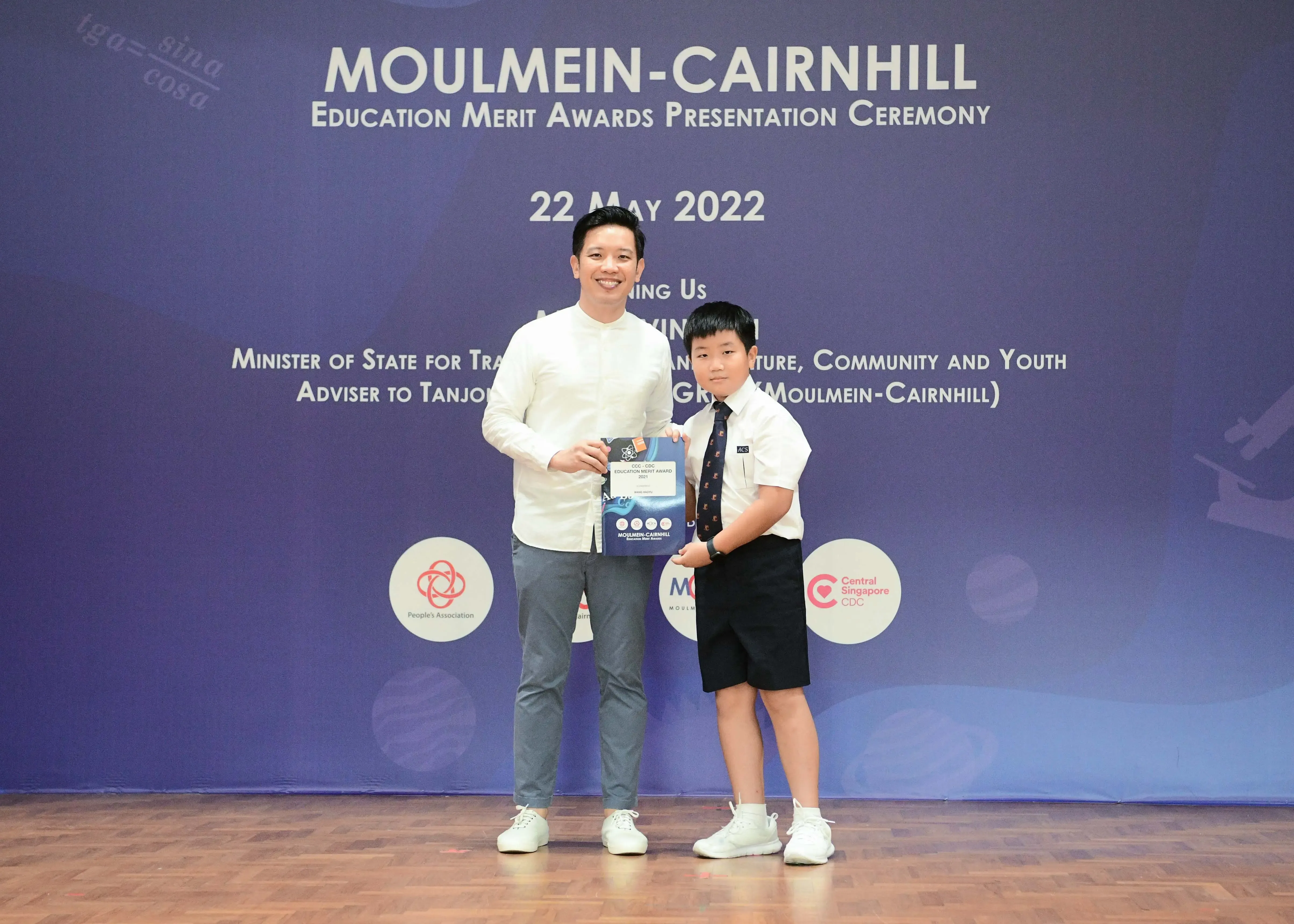 A man and a young boy in school uniform hold an award together at the Moulmein-Cairnhill Education Merit Awards ceremony on 22 May 2022.