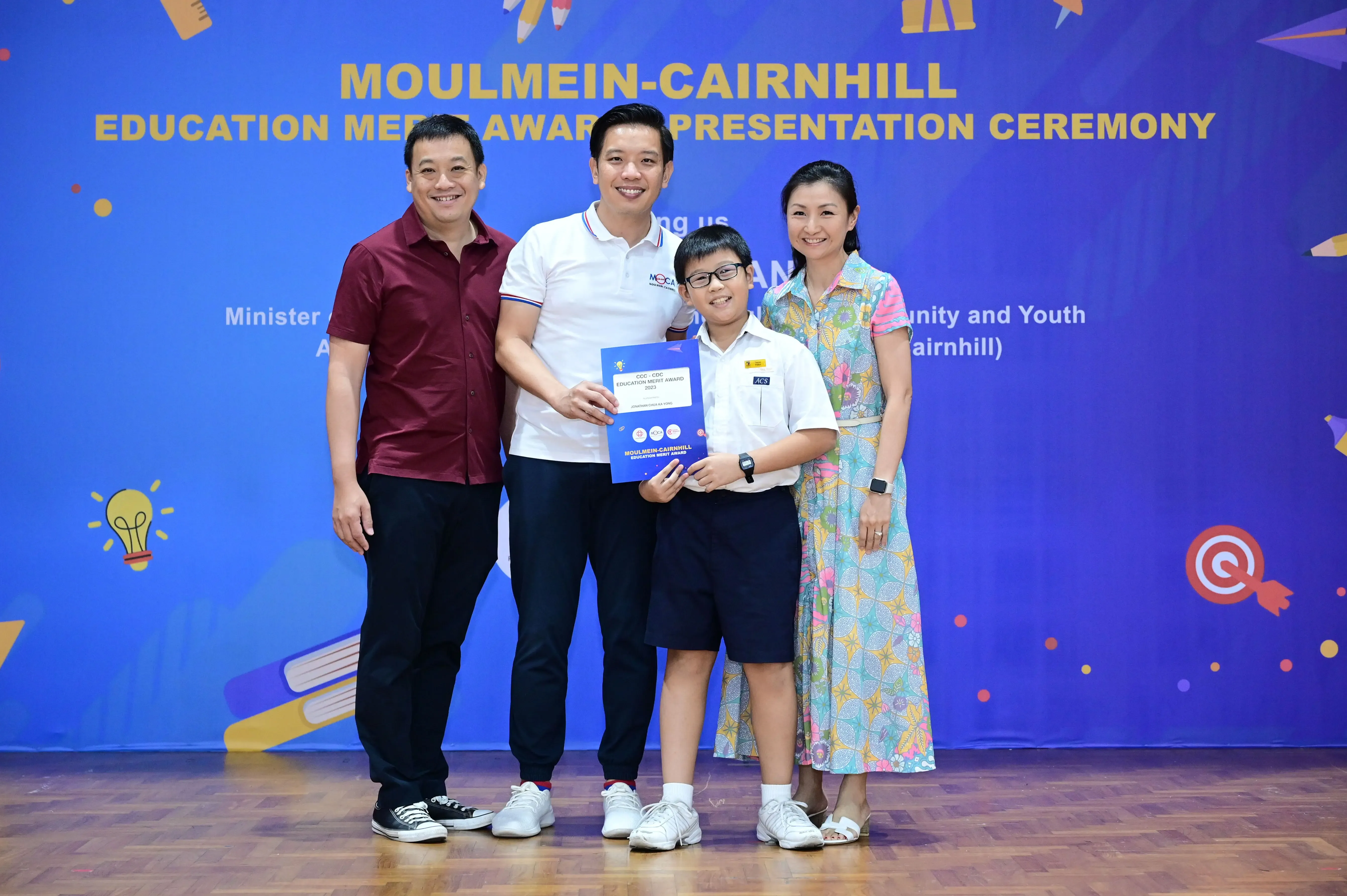 Three adults and a boy holding a certificate pose at the Moulmein-Cairnhill Education Merit Award Presentation Ceremony.
