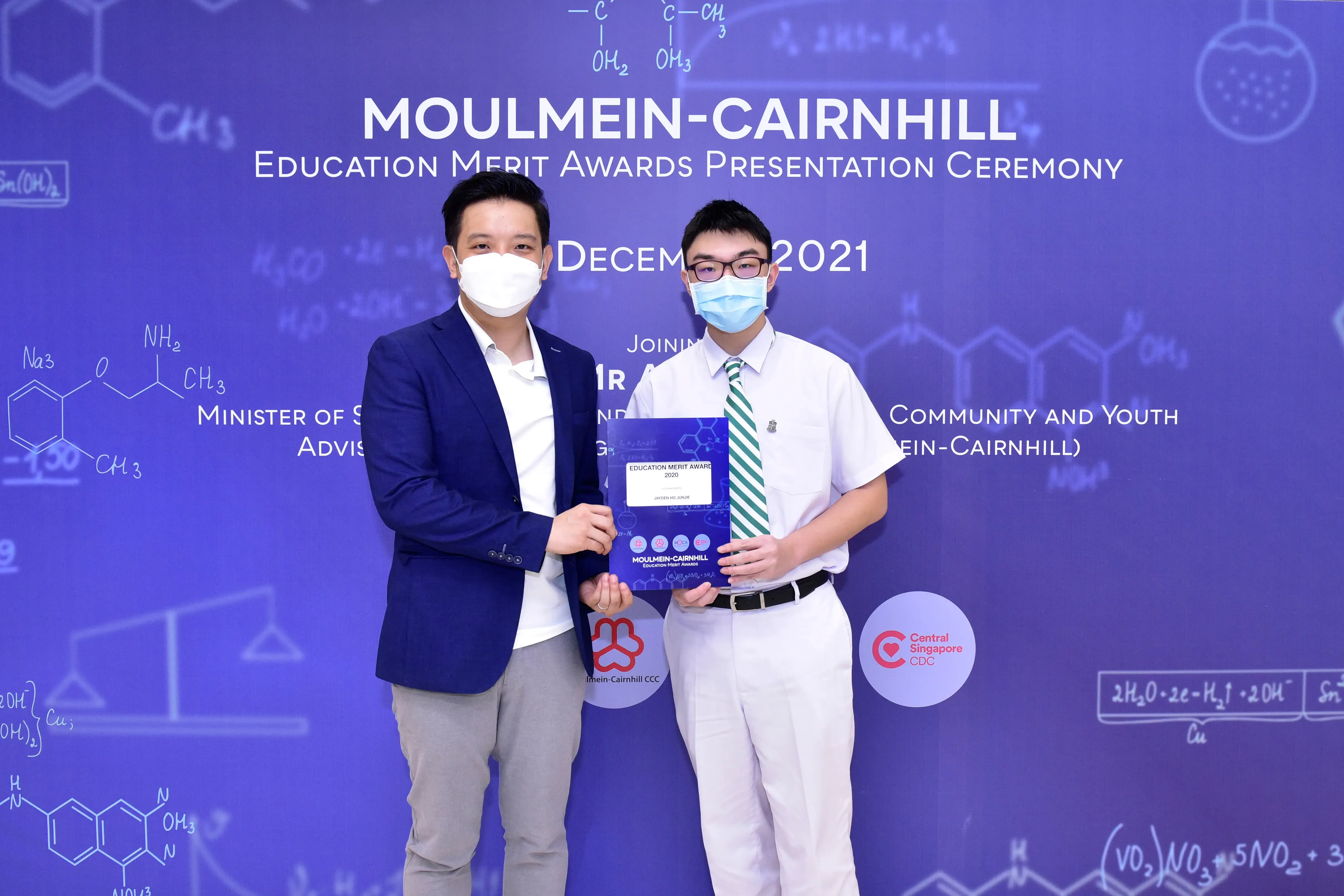 Two masked men hold an award plaque at the Moulmein-Cairnhill Education Merit Awards Presentation Ceremony, December 2021.