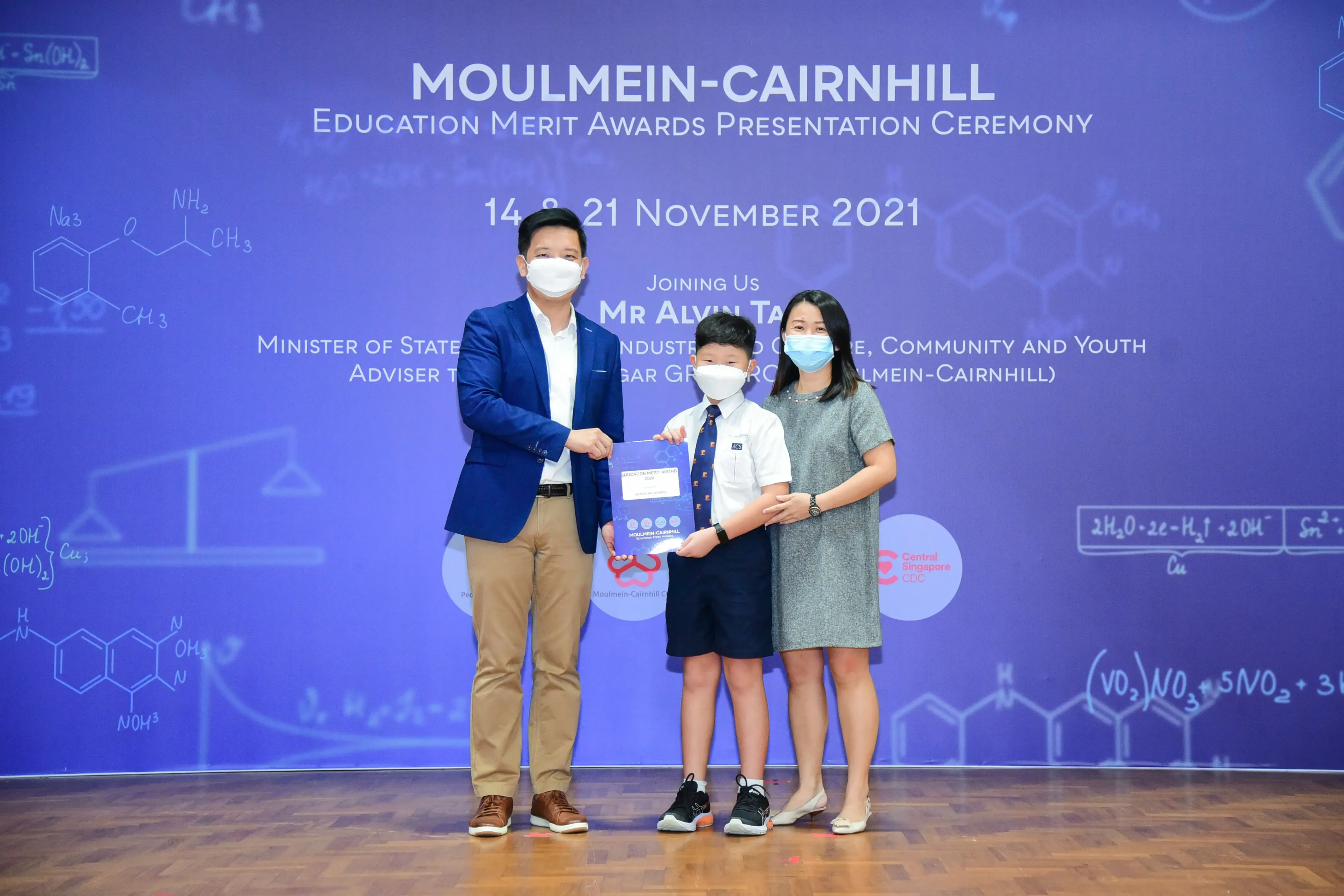 Three masked people hold an award at the Moulmein-Cairnhill Education Merit Awards Ceremony, November 2021.