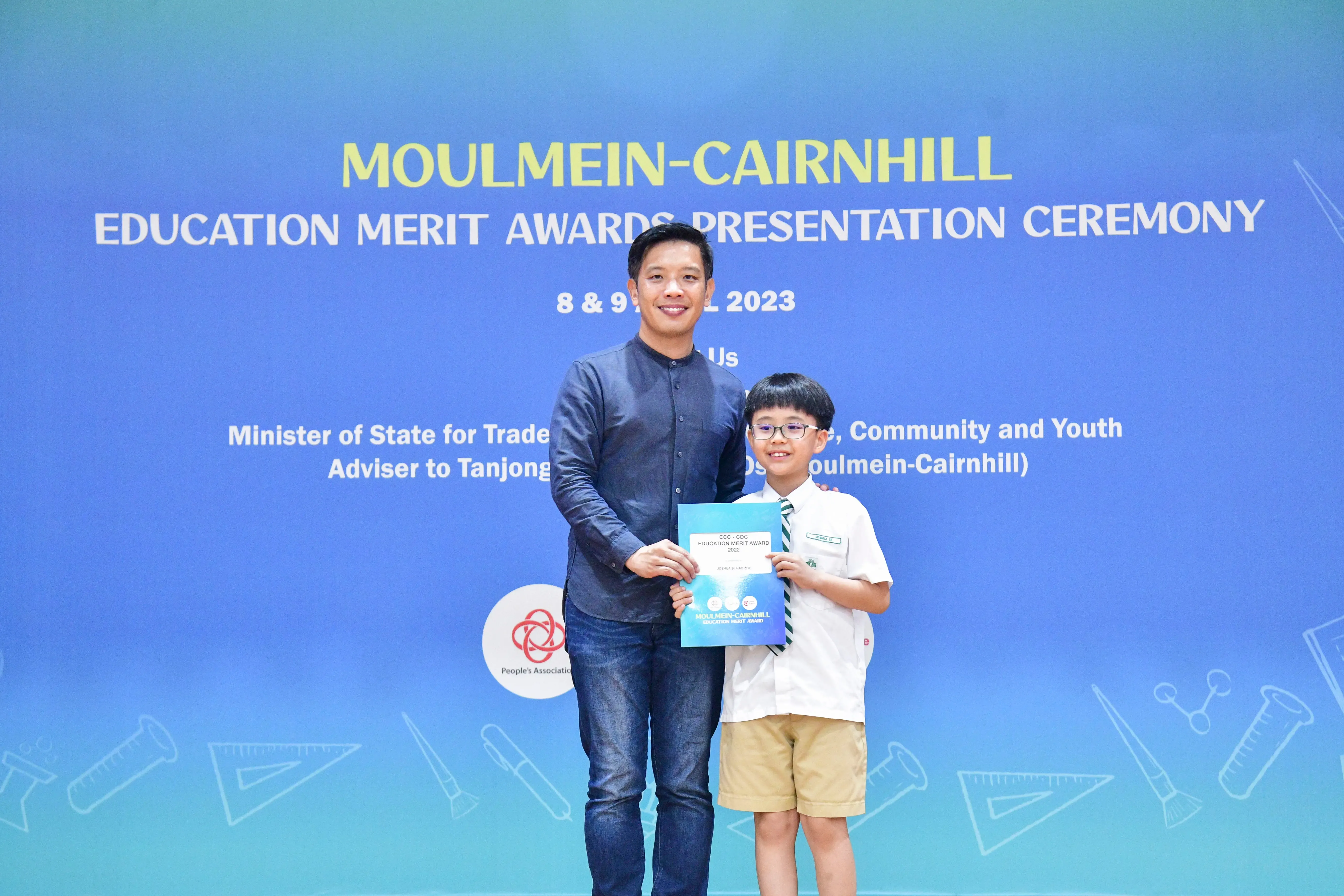 Adult man and young boy in school uniform hold a certificate at Moulmein-Cairnhill Education Merit Awards 2023.