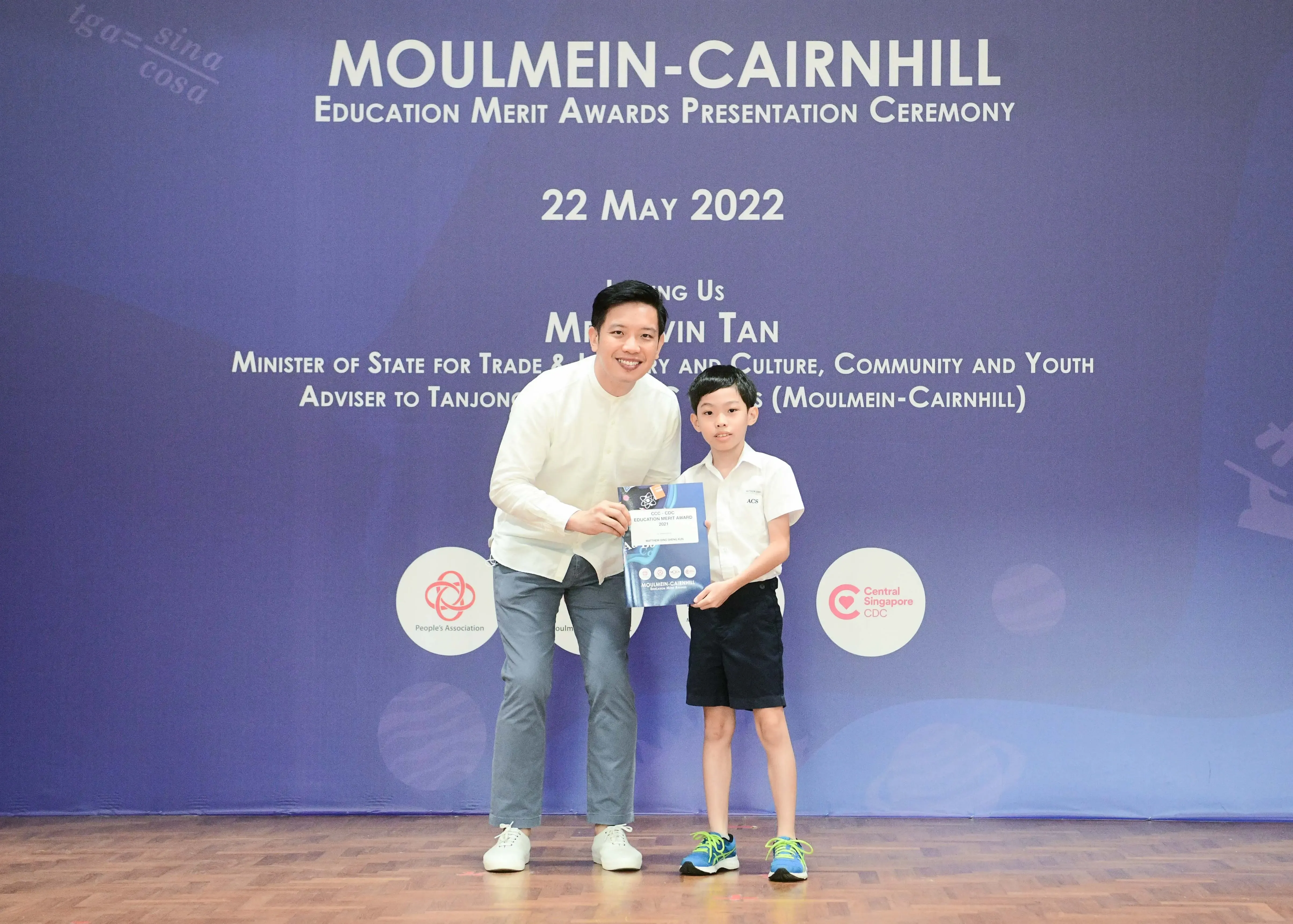 A man and a young boy hold an award certificate at the Moulmein-Cairnhill Education Merit Awards Ceremony on 22 May 2022.