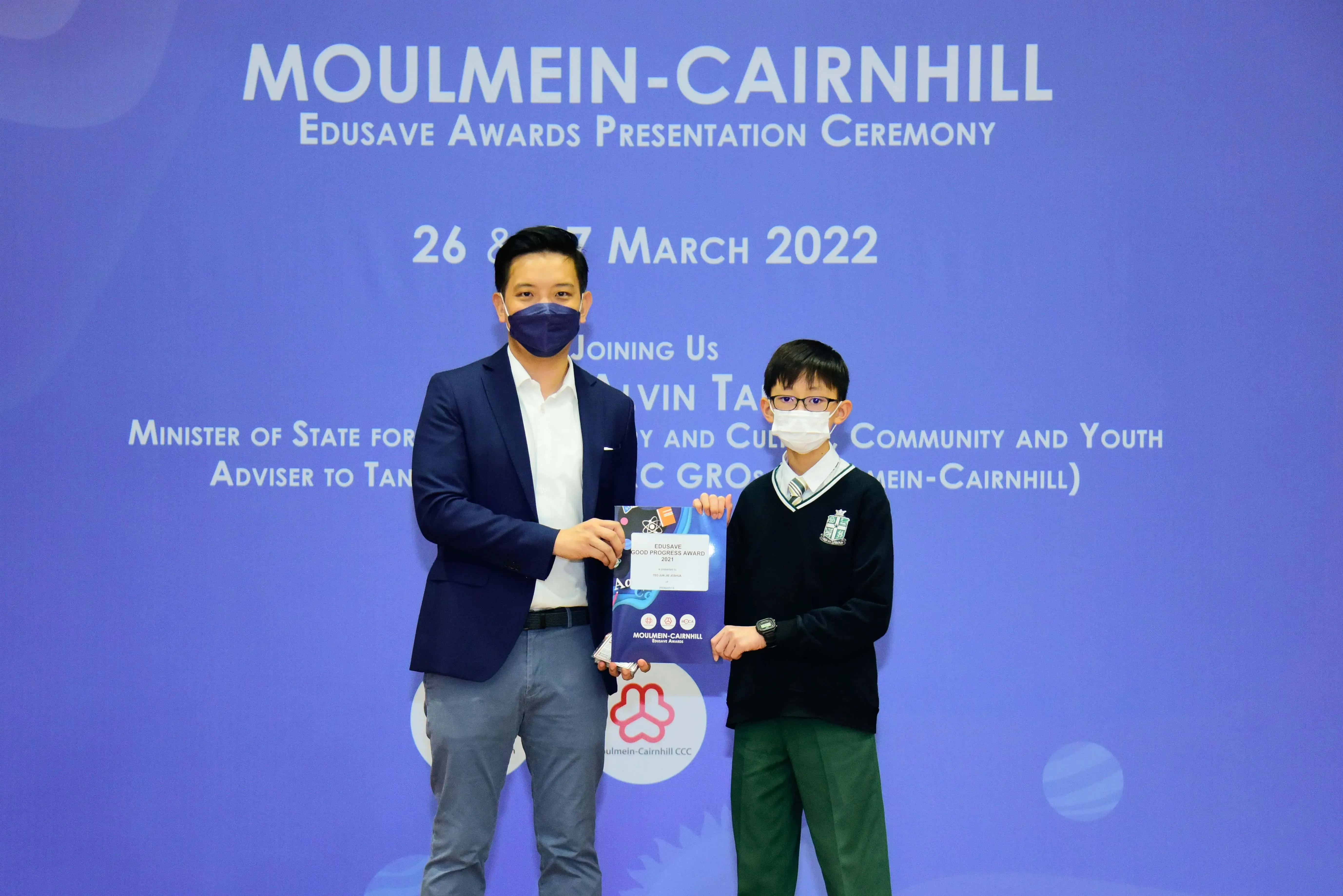 An adult and a masked student hold an award certificate at the Moulmein-Cairnhill Edusave Awards Ceremony 2022.