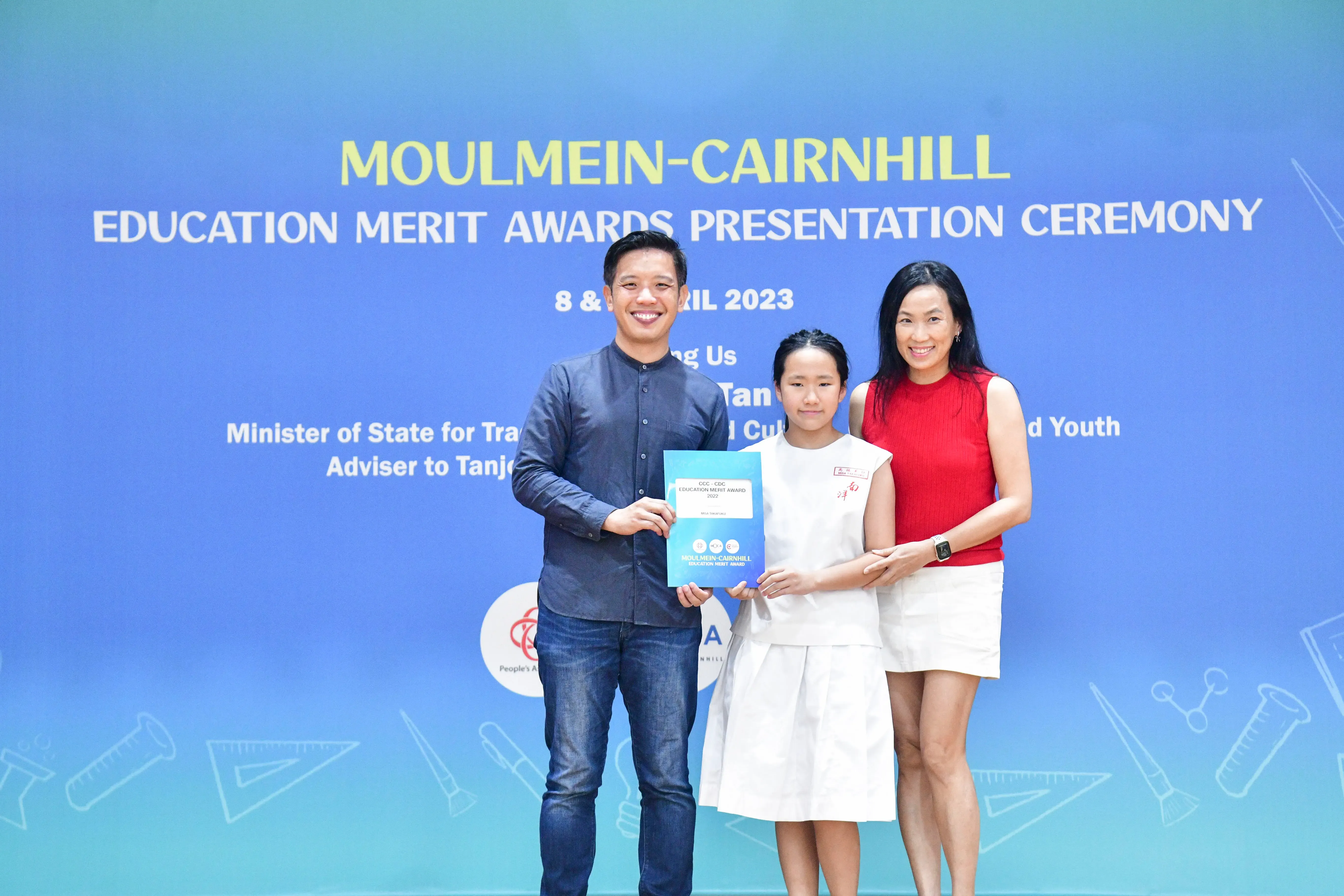 Three people pose holding a certificate at the Moulmein-Cairnhill Education Merit Awards Presentation Ceremony, April 2023.