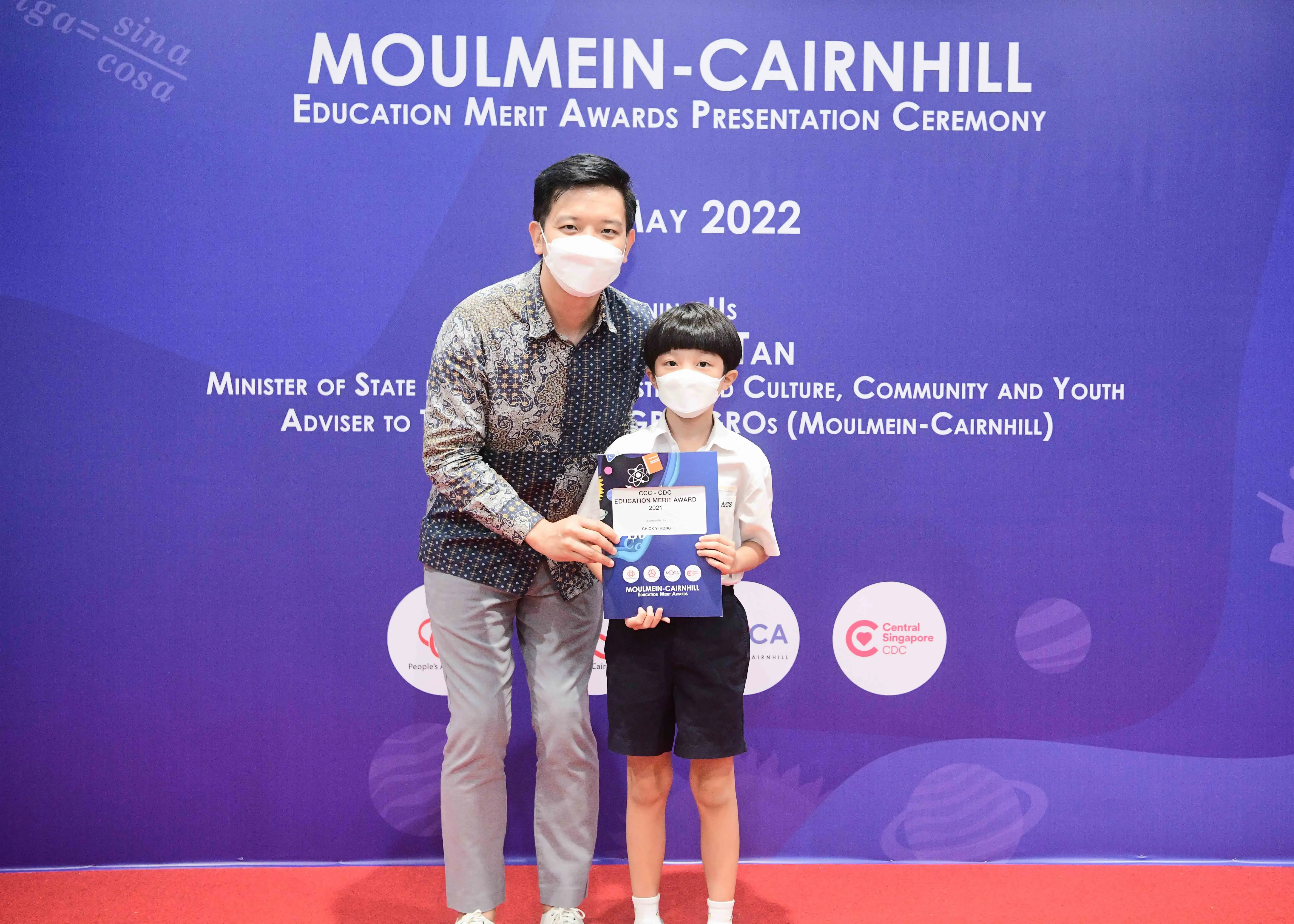 An adult and a young boy wearing masks hold an award certificate at the Moulmein-Cairnhill Education Merit Awards 2022.