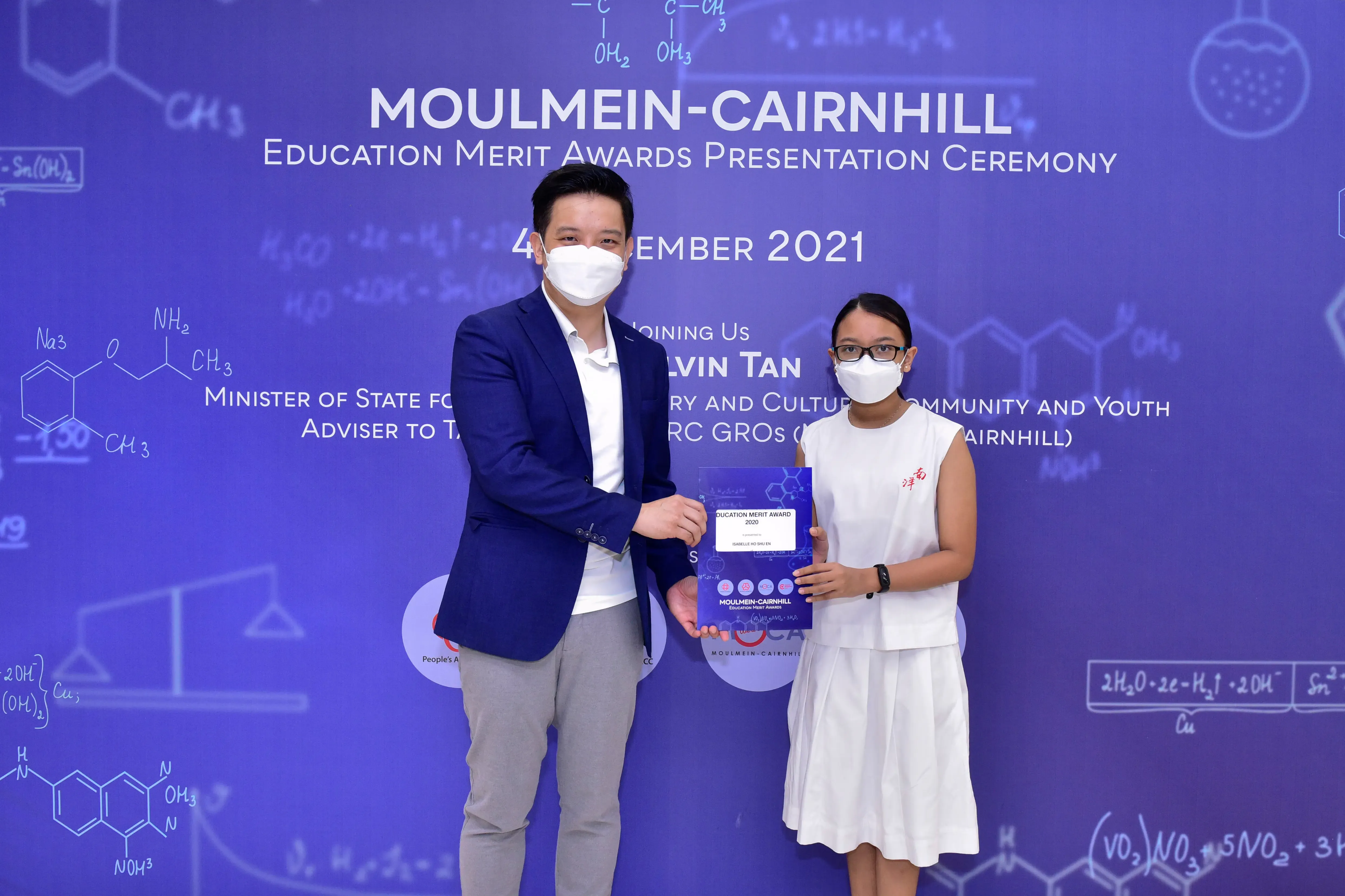 Two masked people hold an award certificate at the Moulmein-Cairnhill Education Merit Awards Ceremony 2021.