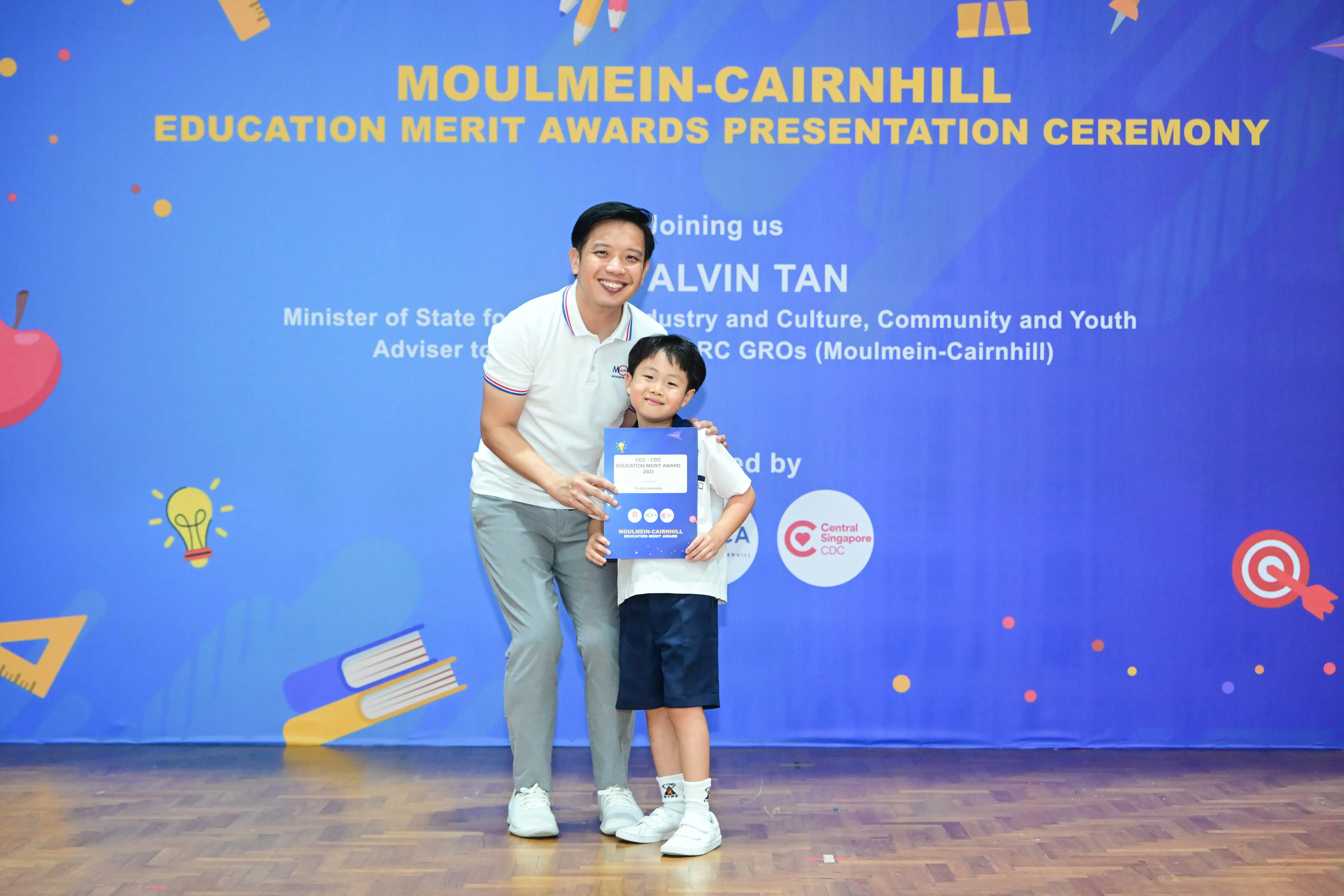 A man and a young boy hold a certificate at the Moulmein-Cairnhill Education Merit Awards Presentation Ceremony.