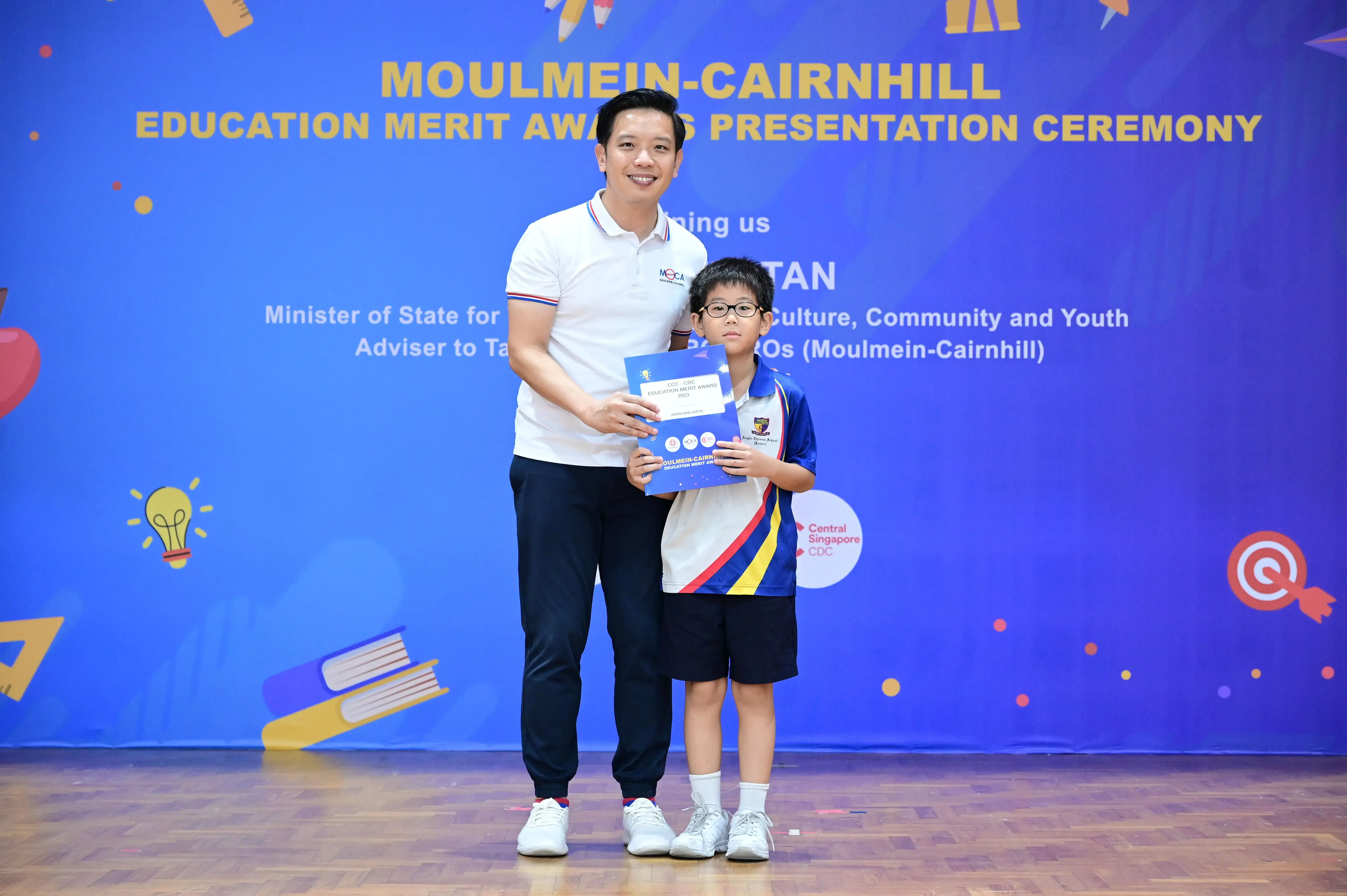 A man and a young boy holding an award booklet at the Moulmein-Cairnhill Education Merit Awards Presentation Ceremony.