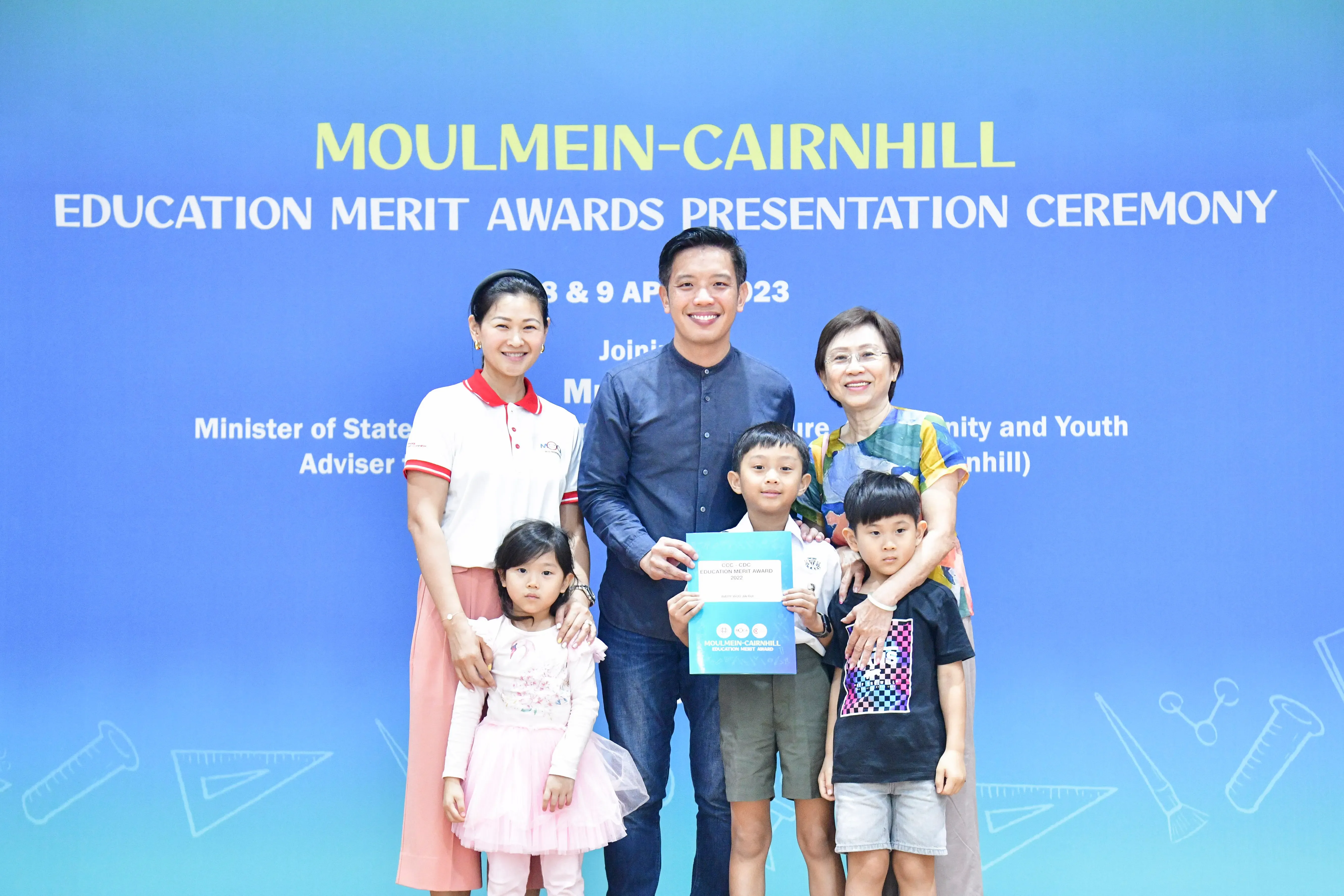 Two women, a man, and three children pose with an award certificate at the Moulmein-Cairnhill Education Merit Awards ceremony.