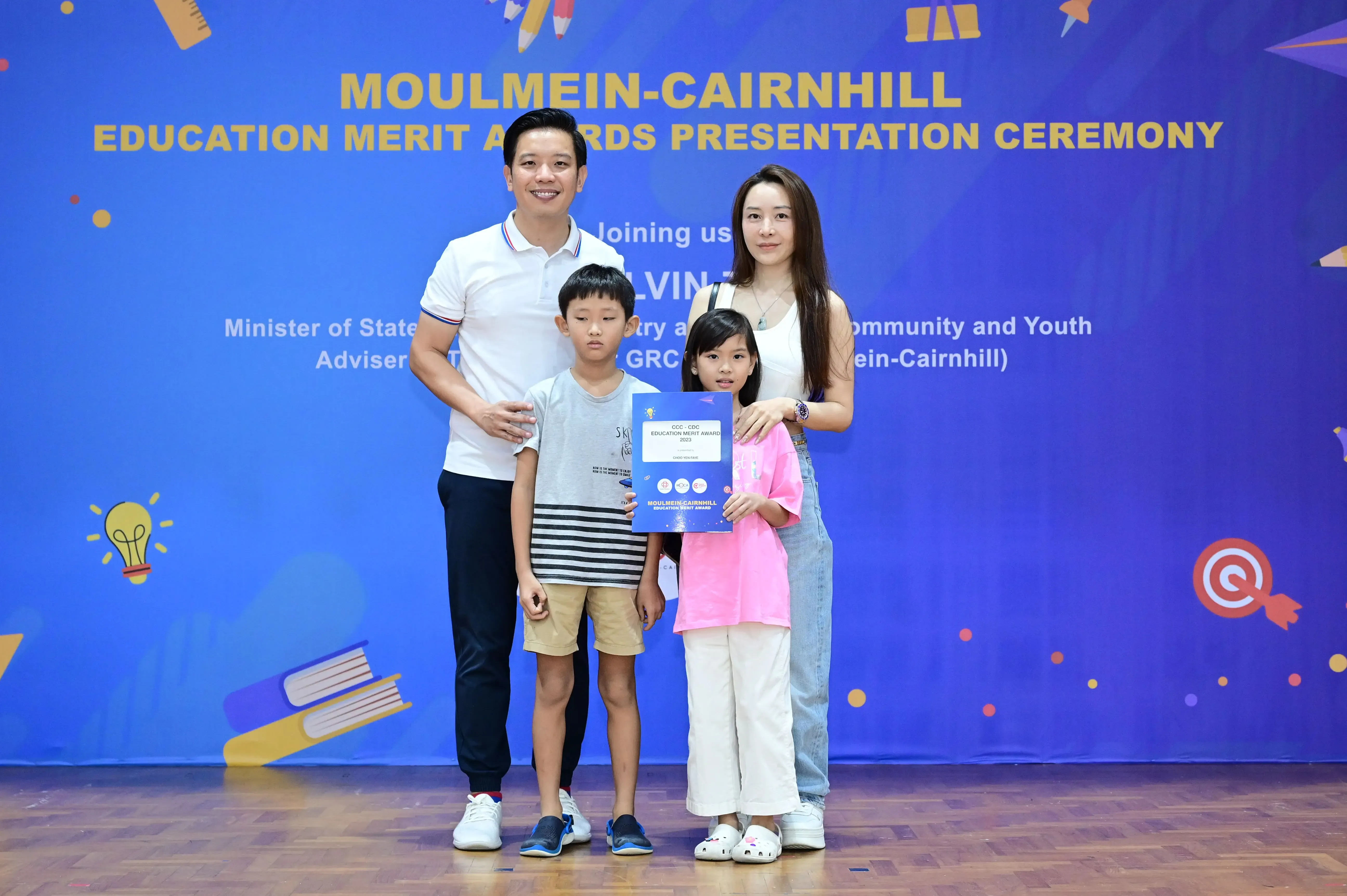 Family of four posing with an award certificate at the Moulmein-Cairnhill Education Merit Awards Presentation Ceremony.