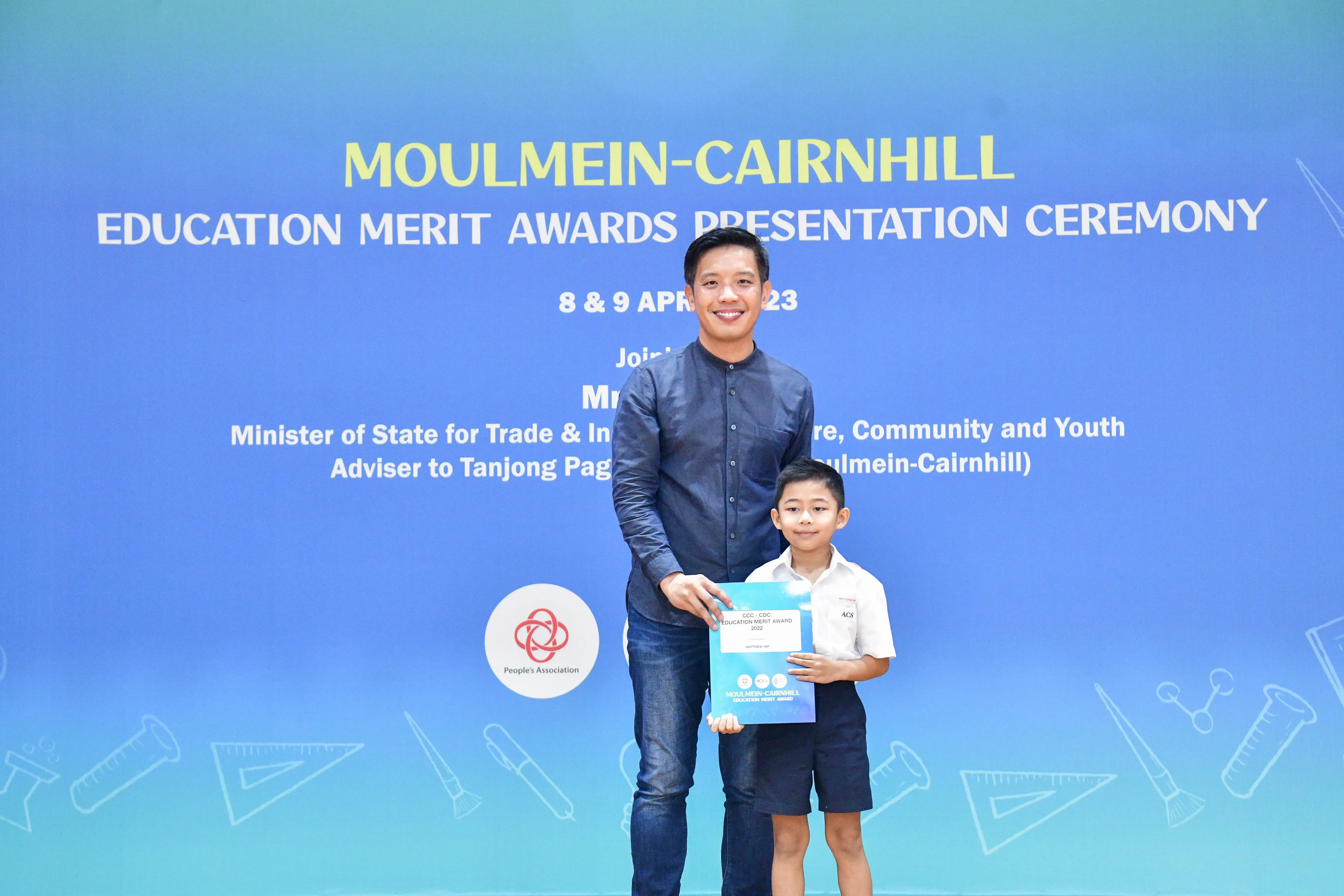 A man and a young boy hold an award certificate at the Moulmein-Cairnhill Education Merit Awards Ceremony.