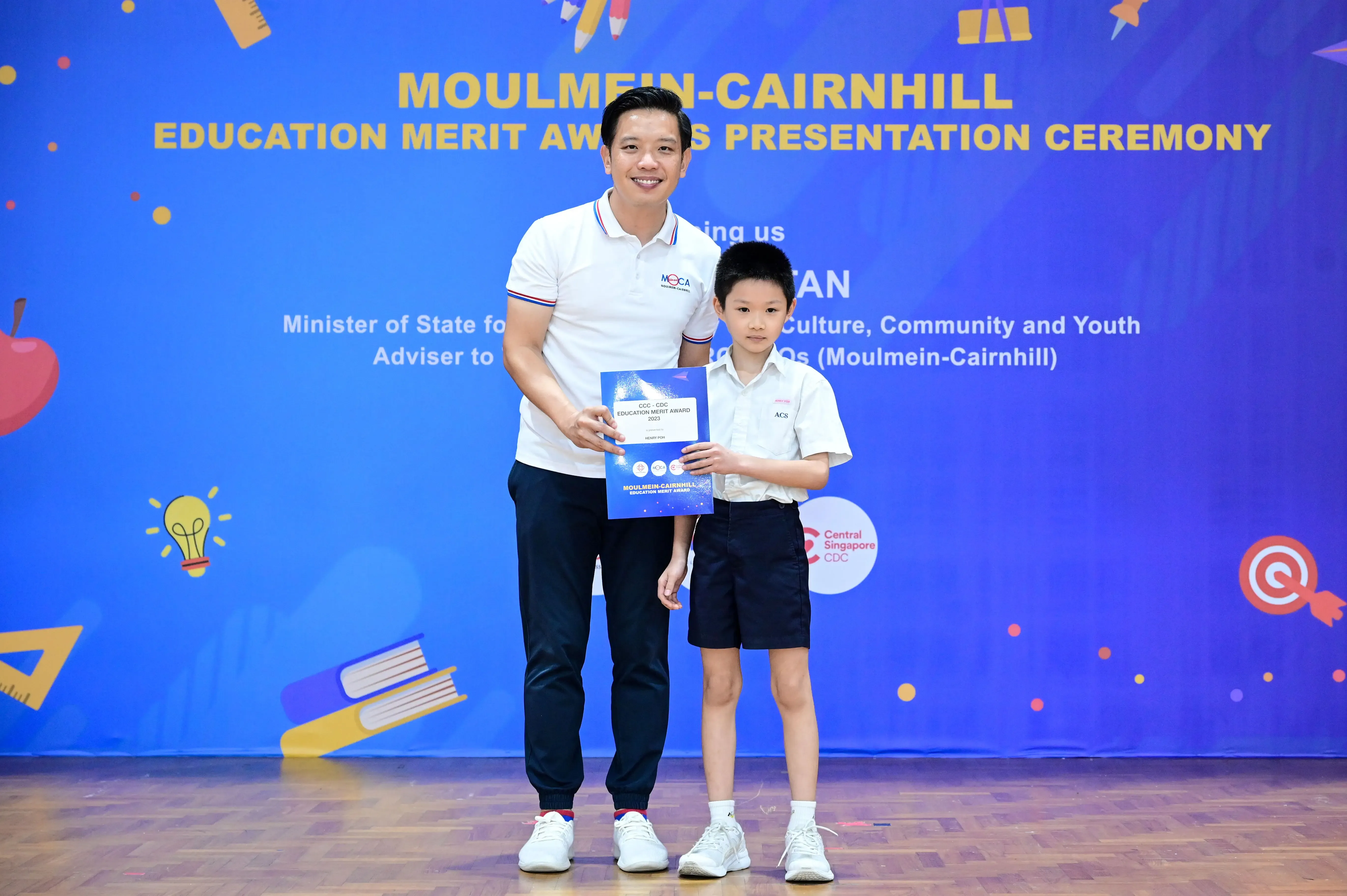 A man and a young boy hold a certificate at the Moulmein-Cairnhill Education Merit Awards Presentation Ceremony.
