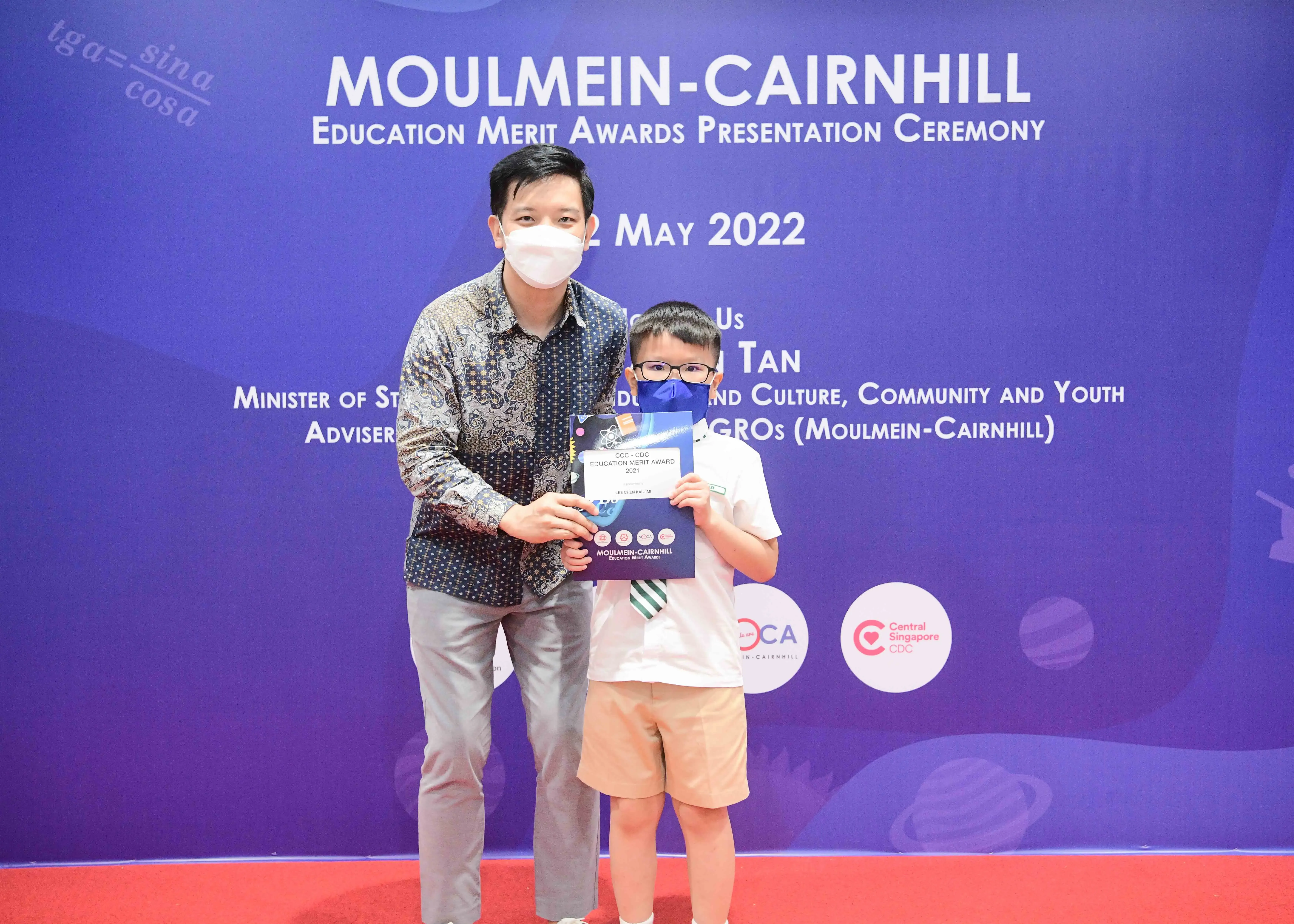 An adult and a young boy wearing masks hold a certificate at the Moulmein-Cairnhill Education Merit Awards 2022.