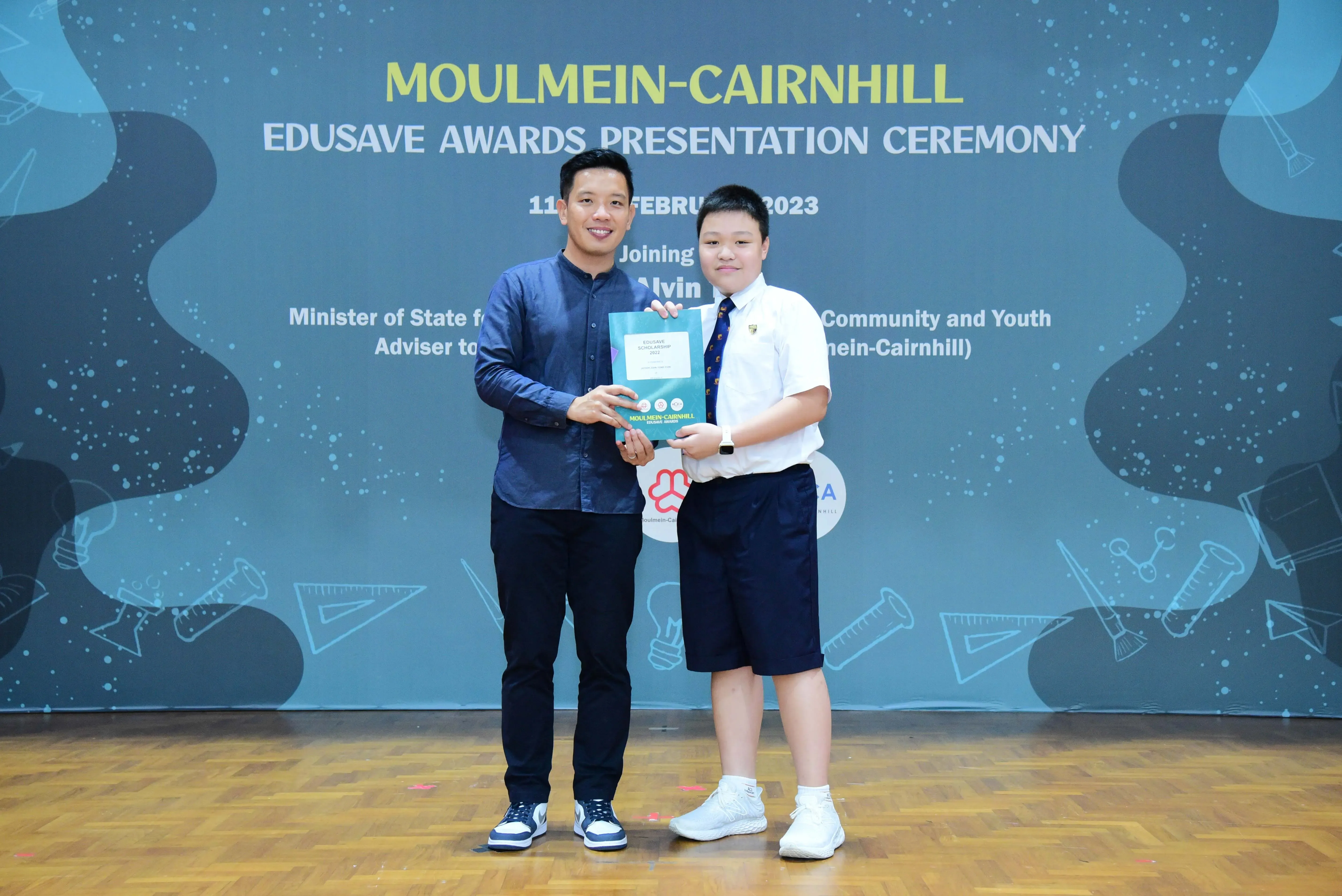 An adult and a student hold an award booklet at the Moulmein-Cairnhill Edusave Awards Presentation Ceremony 2023.