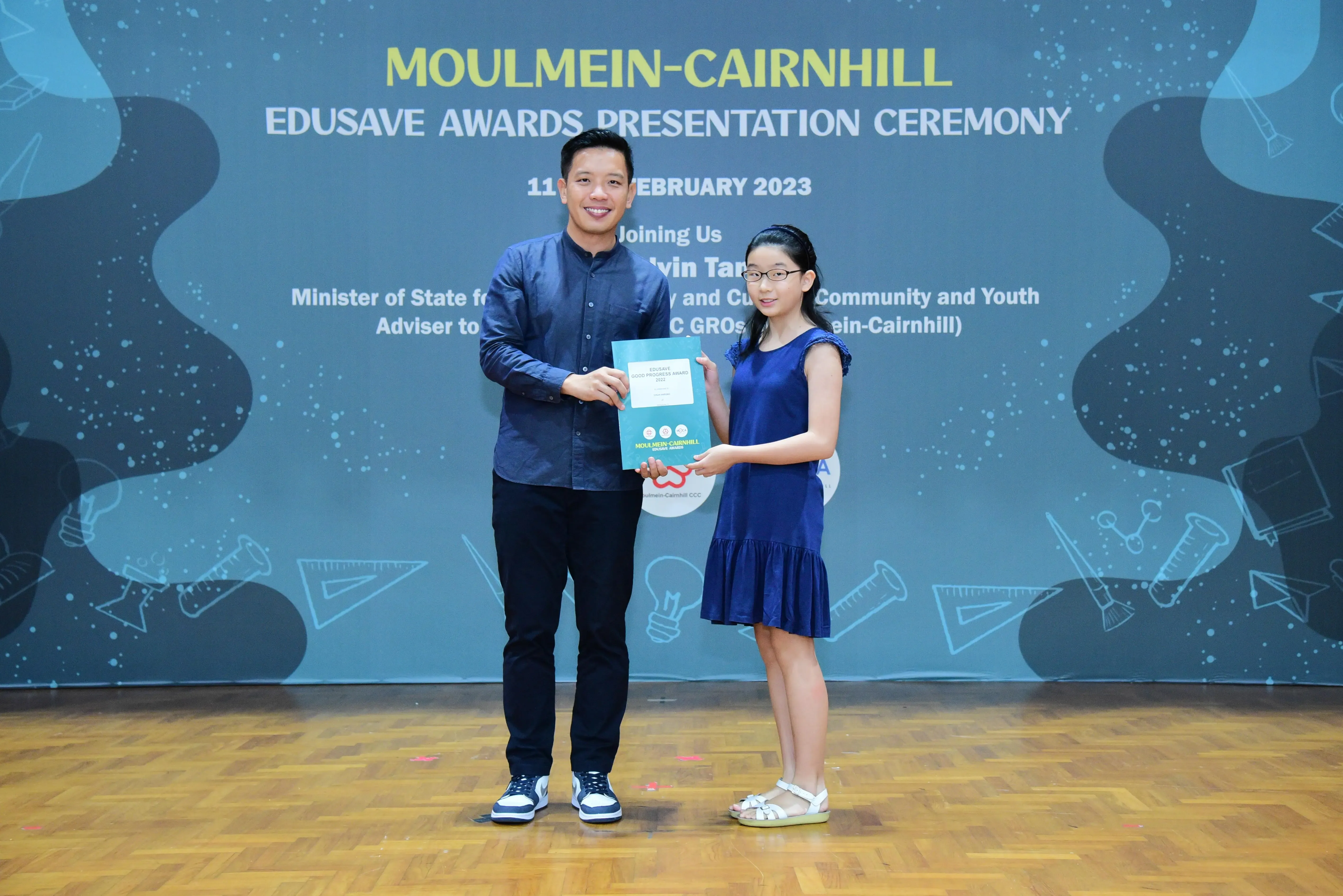 A man and a young girl hold a certificate together at the Moulmein-Cairnhill Edusave Awards Ceremony 2023.