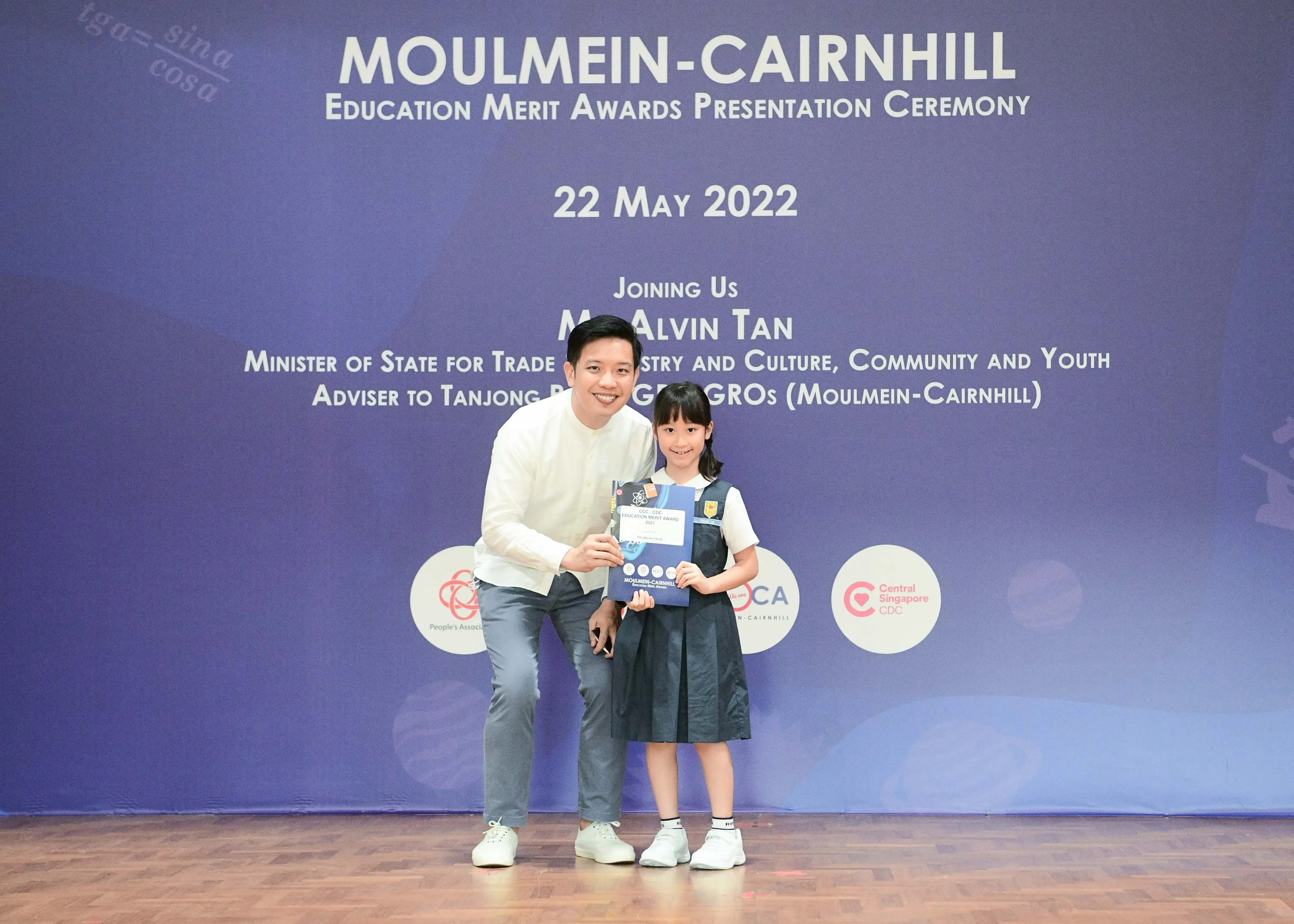 A man and a young girl in school uniform hold an award certificate at the Moulmein-Cairnhill Education Merit Awards 2022.