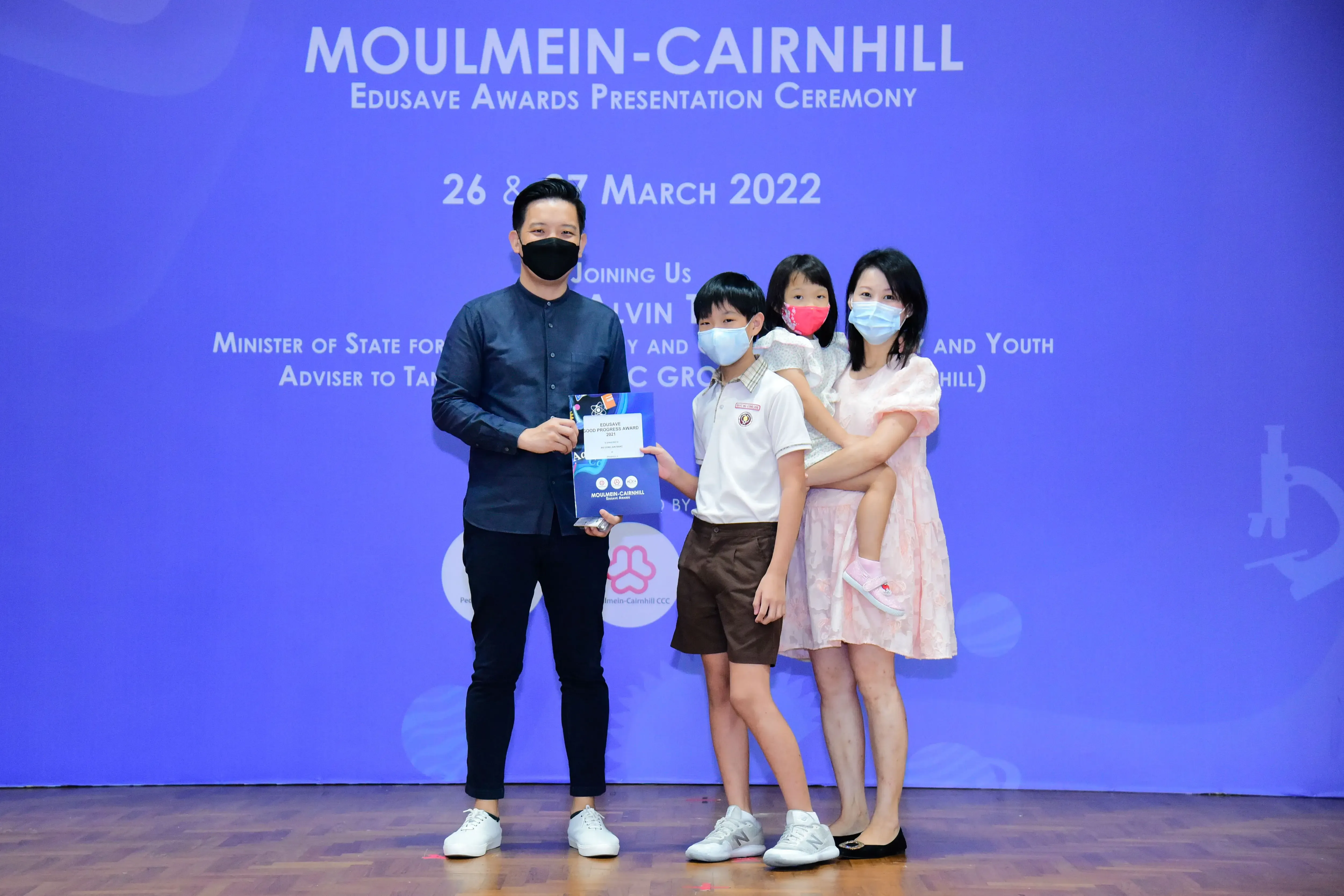 A man, woman, and two children wearing masks pose with an award at the Moulmein-Cairnhill Edusave Awards Ceremony 2022.