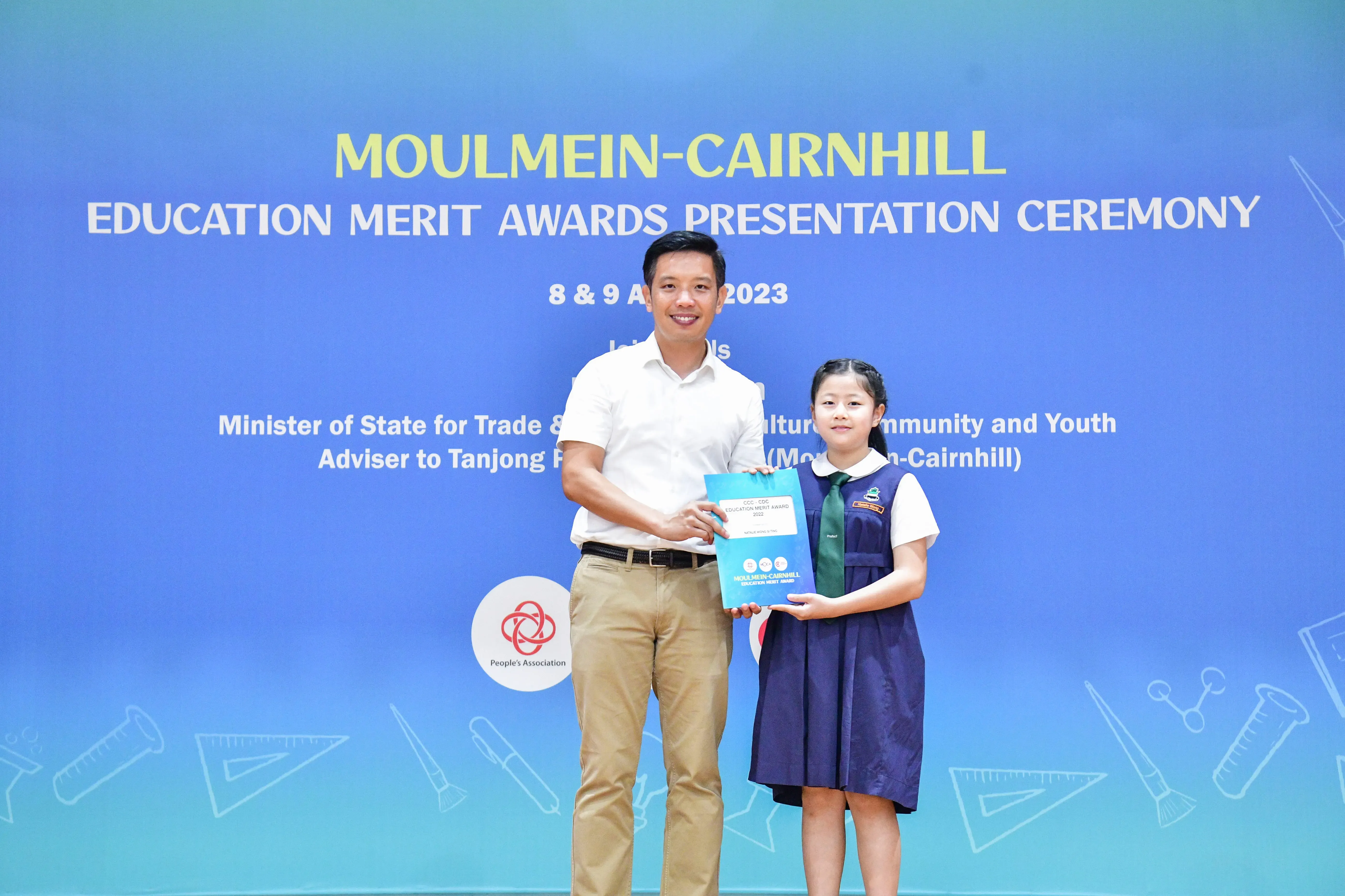 A man and a young girl in school uniform hold an award together at the Moulmein-Cairnhill Education Merit Awards 2023.
