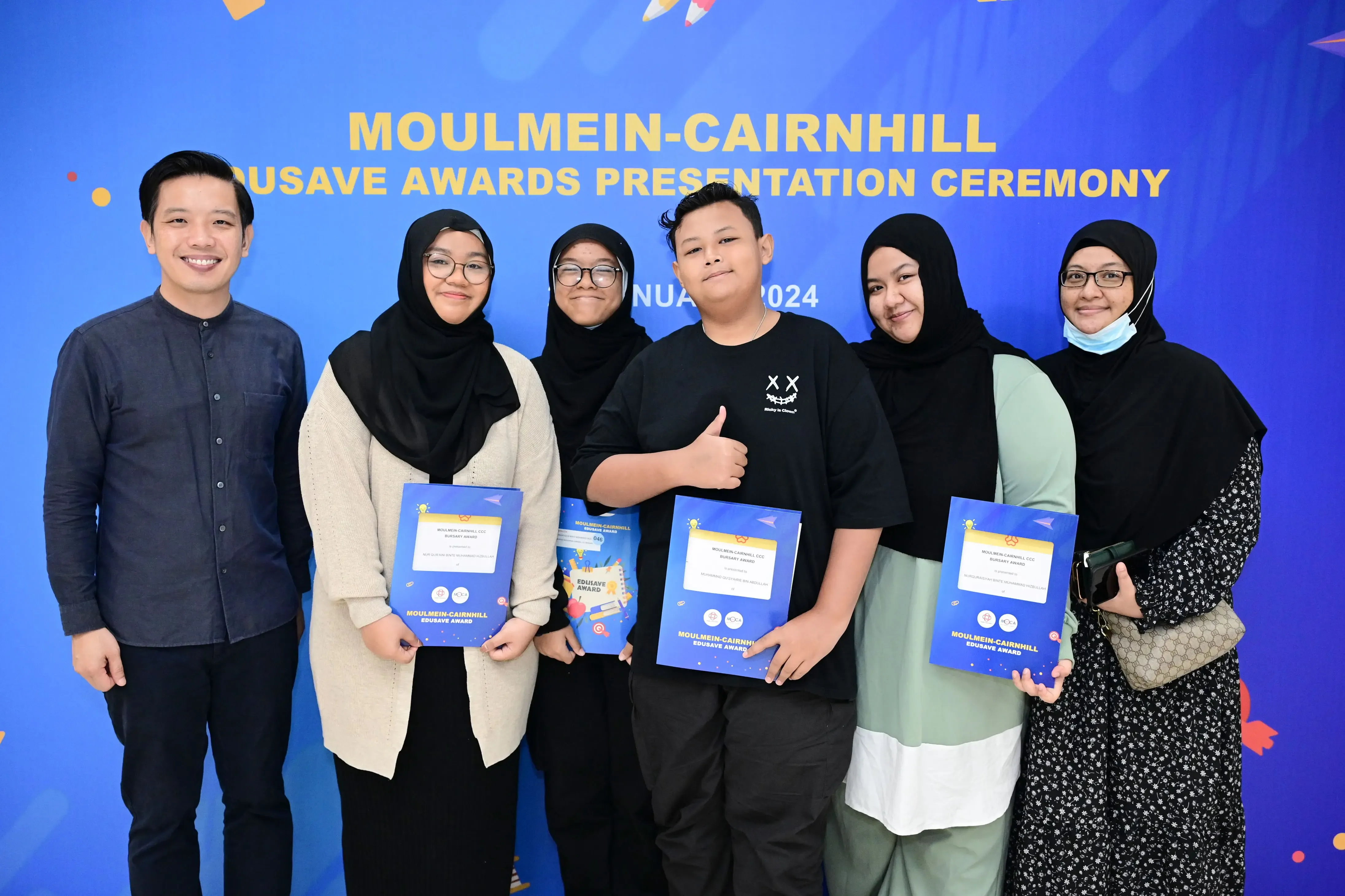 Six people pose holding award folders at the 2024 Moulmein-Cairnhill Edusave Awards Presentation Ceremony.