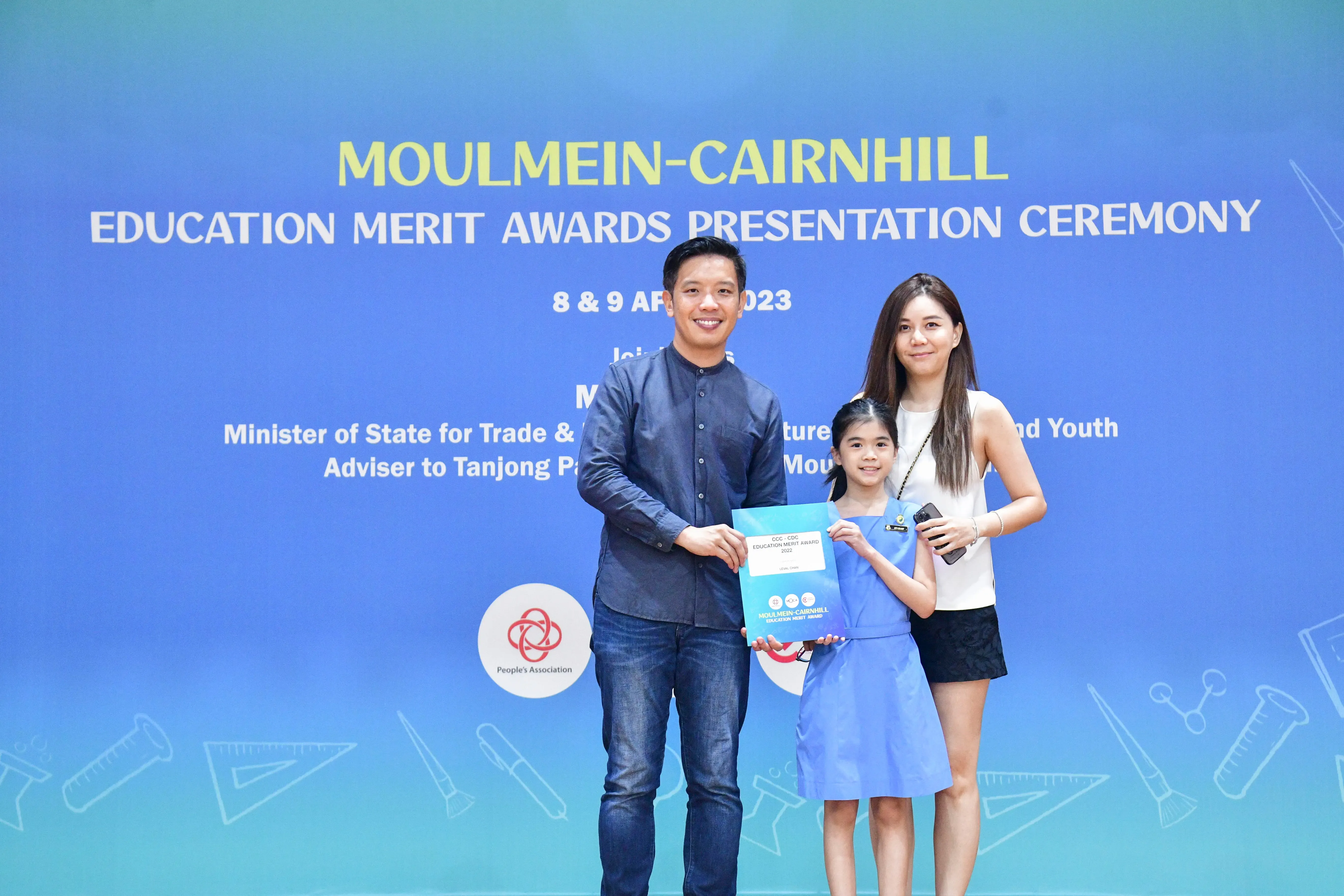 A man, girl, and woman pose with an award certificate at the Moulmein-Cairnhill Education Merit Awards 2023.